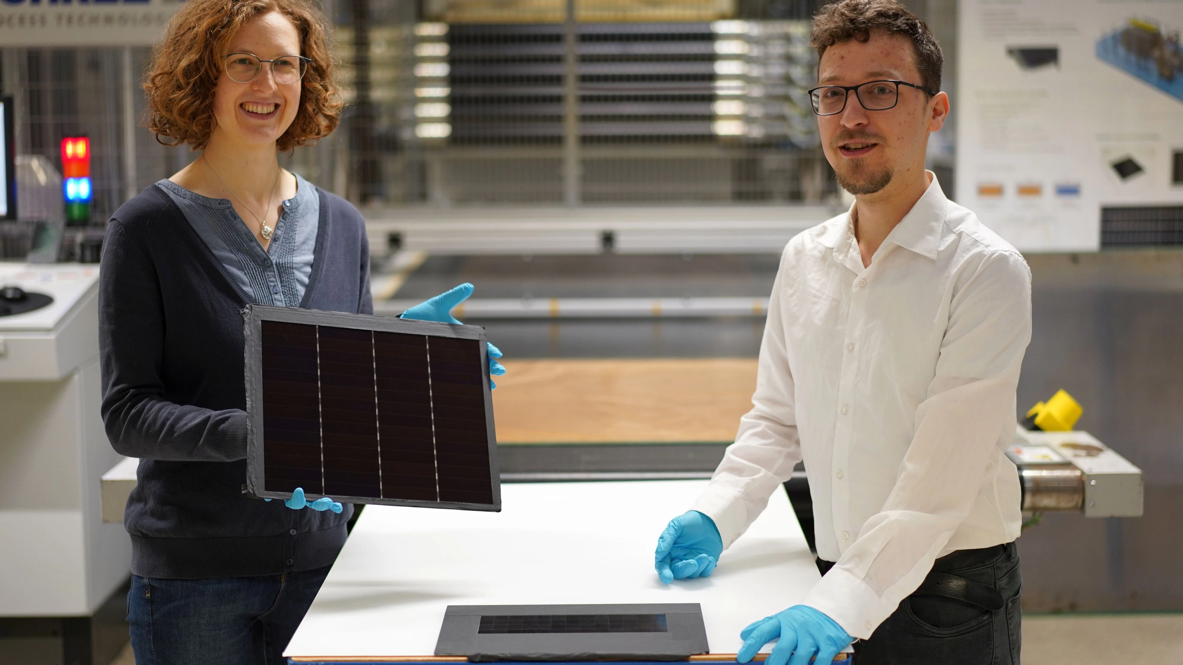 Projektleiterin Dr. Laura Stevens zeigt eines der III-V-Germanium-PV-Module mit einer Rekordeffizienz von 34,2 Prozent. Leonhard Böck ist Projektmitarbeiter und hat maßgeblich am – vor ihm liegenden – III-V-Silizium-PV-Modul mit 31,3 Prozent Effizienz mitgearbeitet.