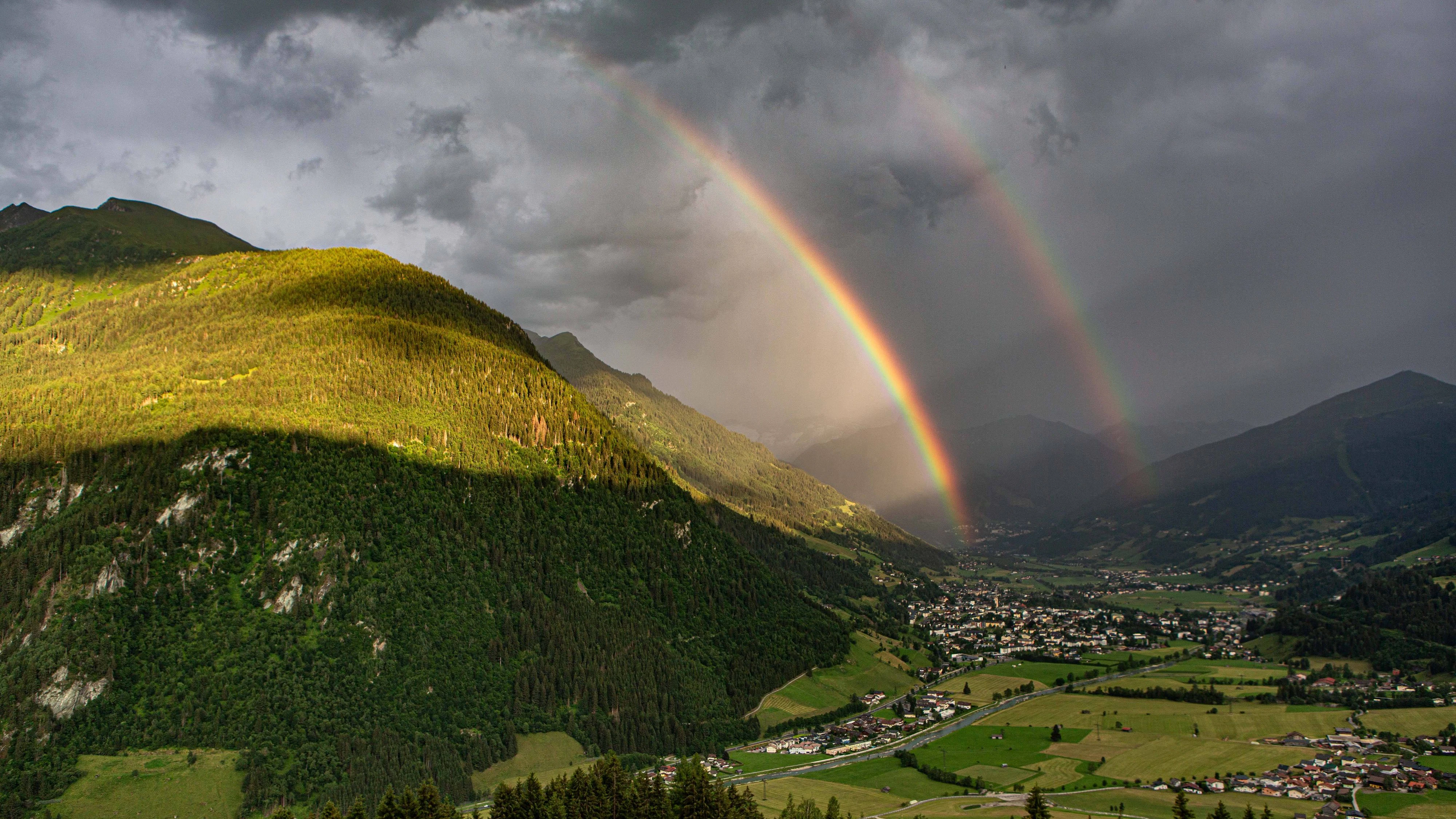 Luftaufnahme des österreichischen Kurorts Bad Hofgastein im Gasteinertal, über dem sich ein markanter Doppelregenbogen vor einer alpinen Bergkulisse erstreckt. (20. Juni 2026)