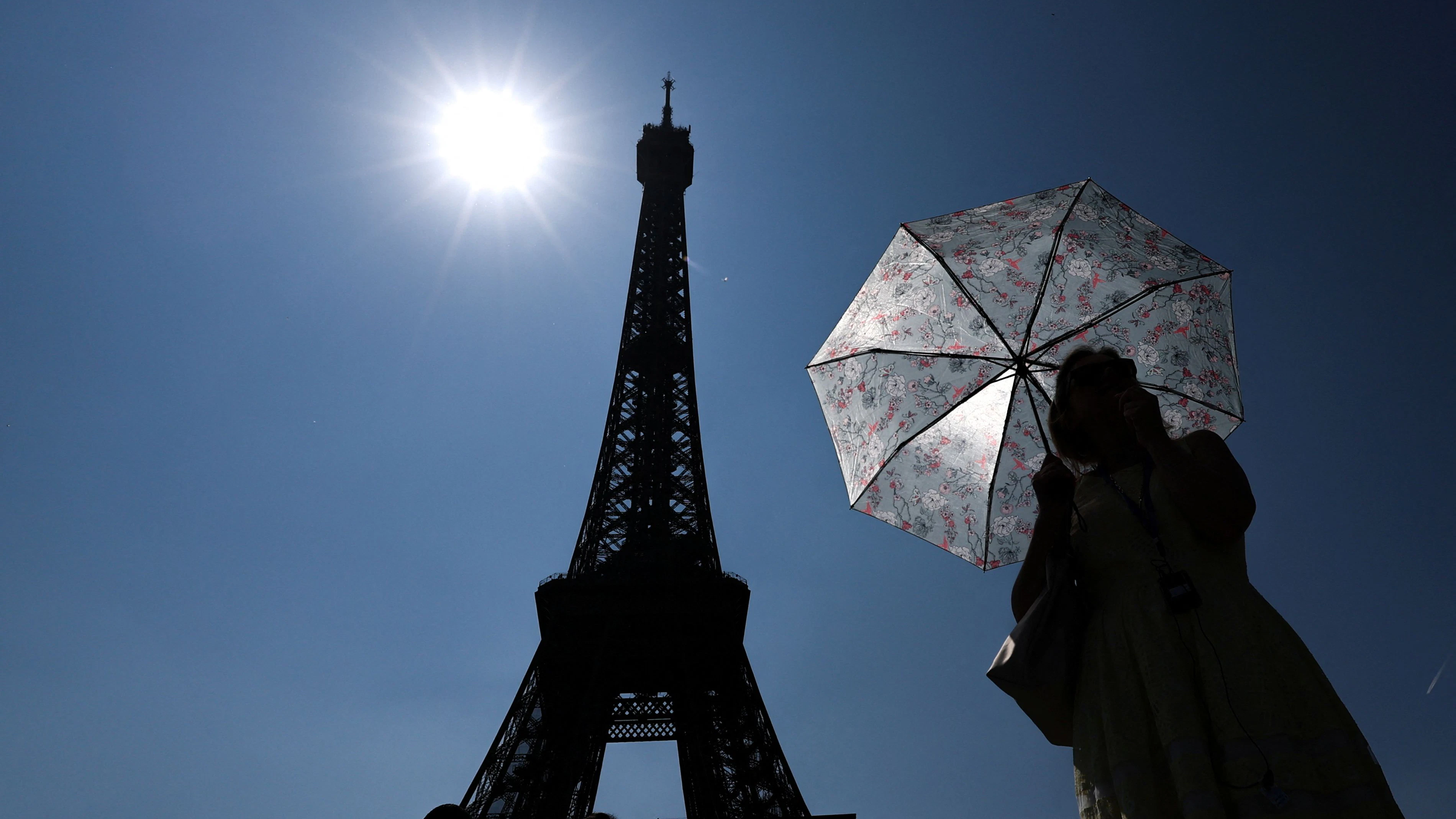 A tourist holding an umbrella to protect herself from the sun stands next to the Eiffel Tower on a warm and sunny spring day in Paris, France, June 19, 2025. REUTERS/Gonzalo Fuentes