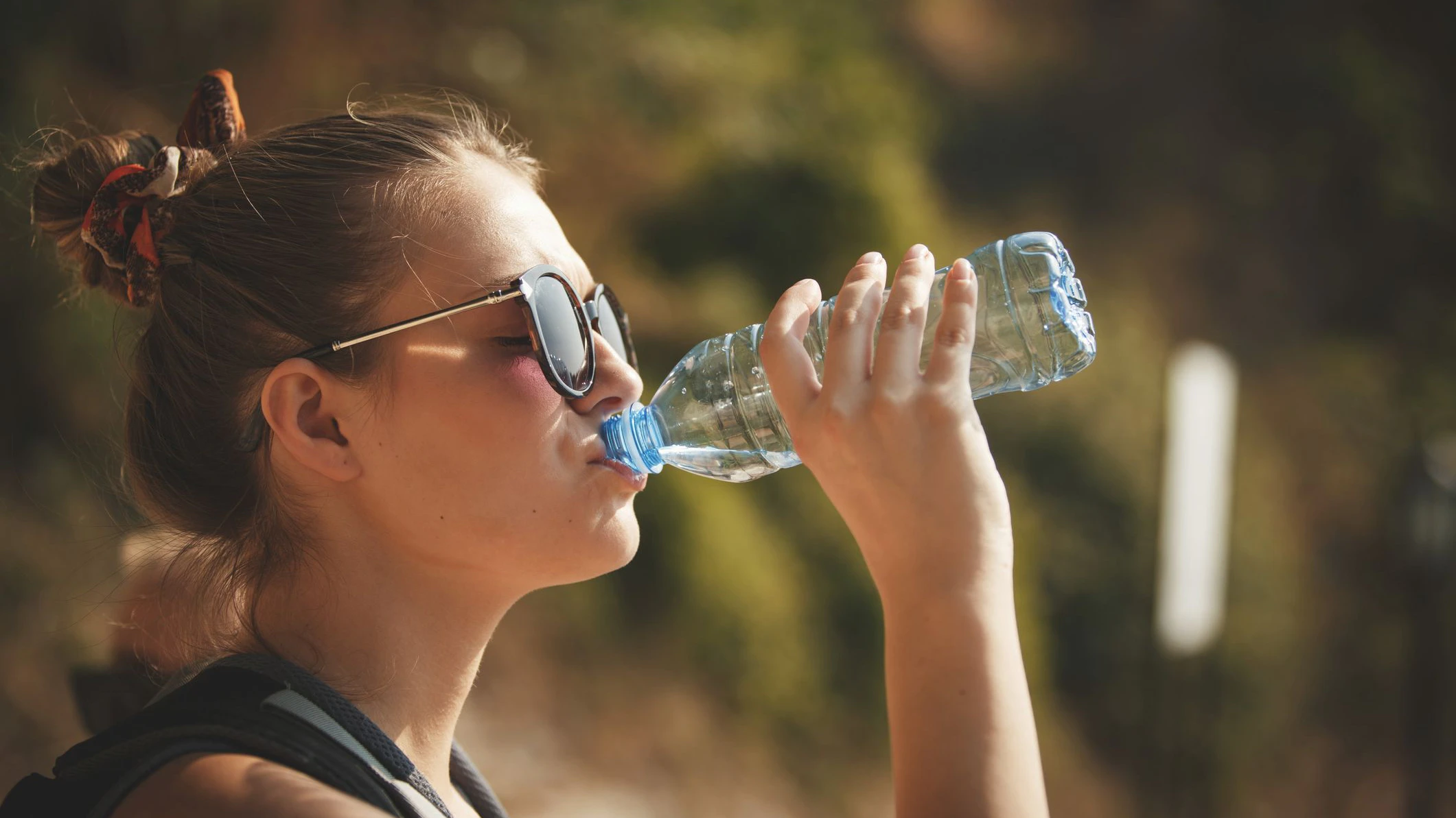 Side view of young woman drinking water from a bottle on a hot summer day.