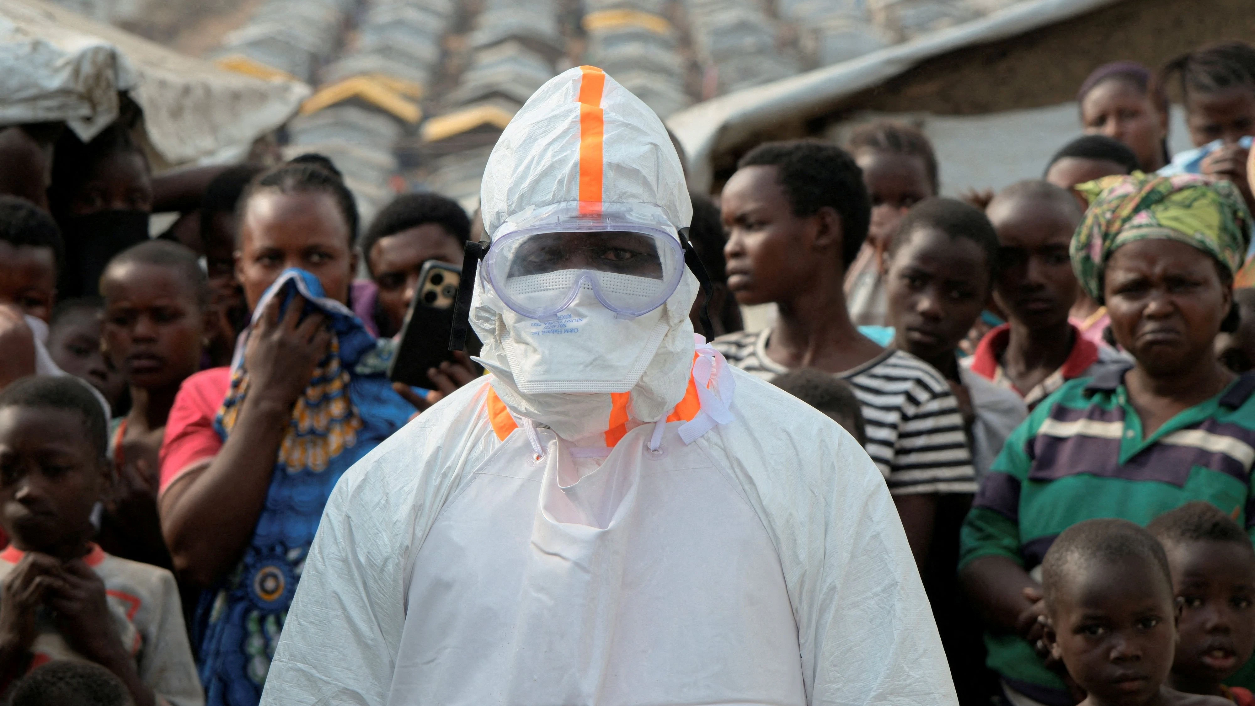 FILE PHOTO: A health worker in personal protective equipment (PPE) stands near displaced people waiting for the burial of suspected Ebola victims at the Kigonze displaced persons camp, one month after an outbreak was declared, in Bunia, eastern Democratic Republic of Congo, June 18, 2026. REUTERS/Gradel Muyisa Mumbere/File Photo
