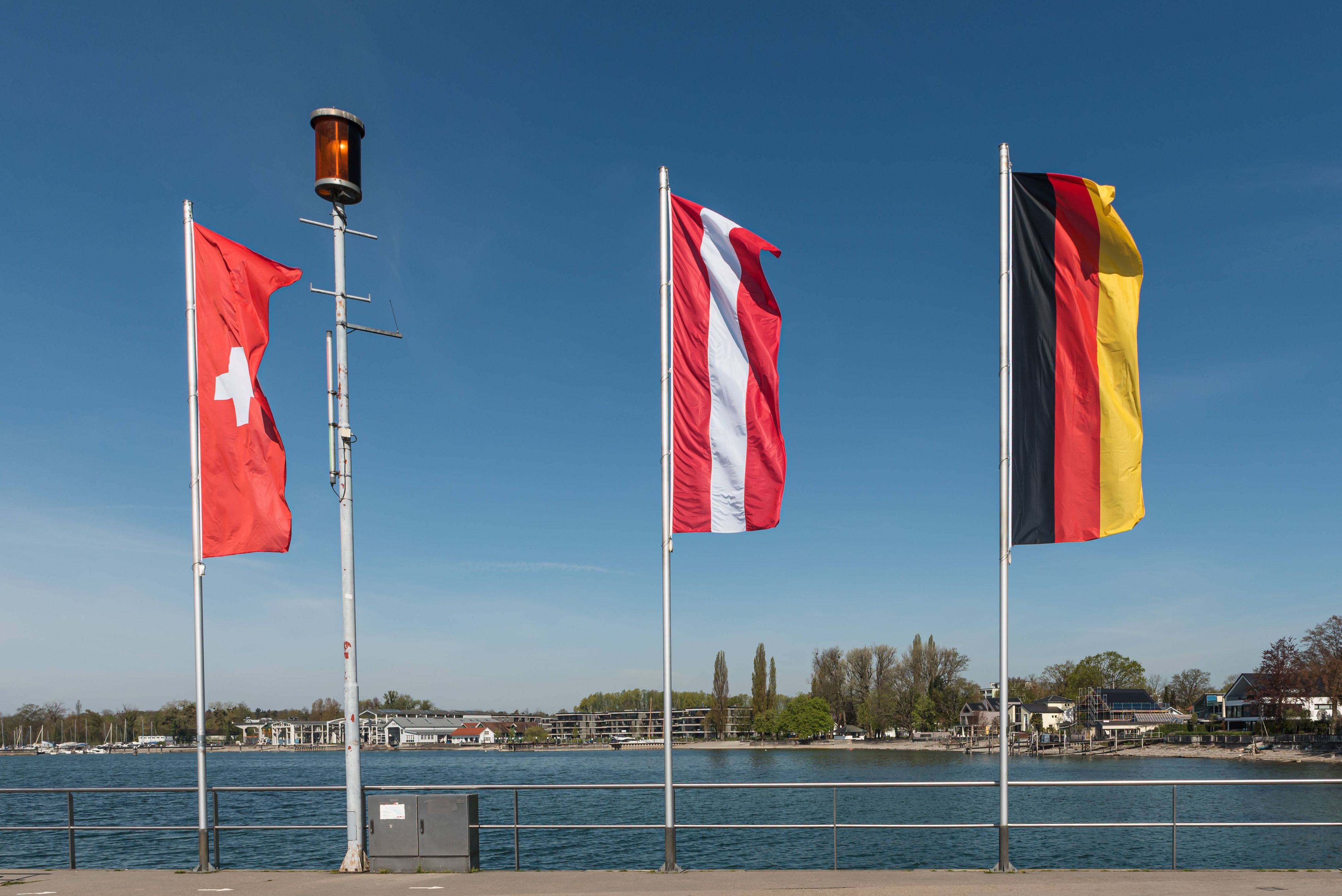 Flaggen von Deutschland, Österreich und der Schweiz im Dreiländereck am Bodensee. Immer mehr Deutsche zieht es in die Schweiz oder nach Österreich.