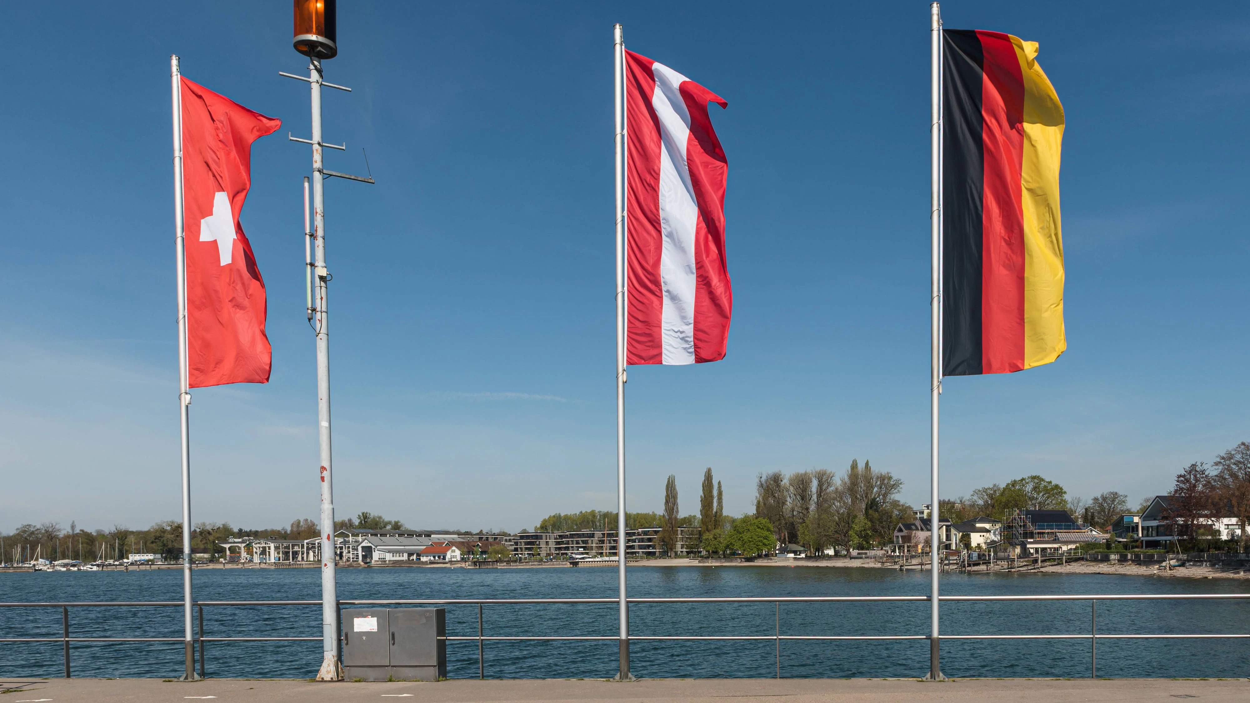 Flaggen von Deutschland, Österreich und der Schweiz im Dreiländereck am Bodensee. Immer mehr Deutsche zieht es in die Schweiz oder nach Österreich.