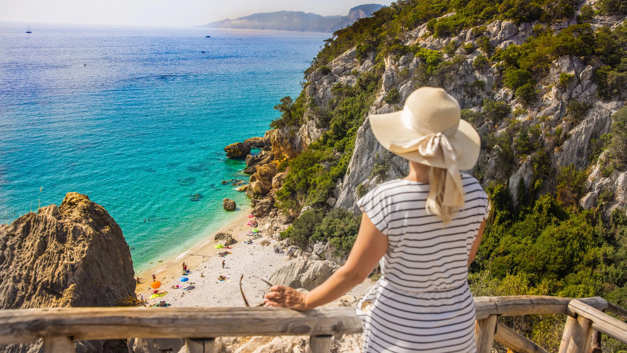 View of a blonde woman looking at the beach from a lookout, Sardinia, Italy.