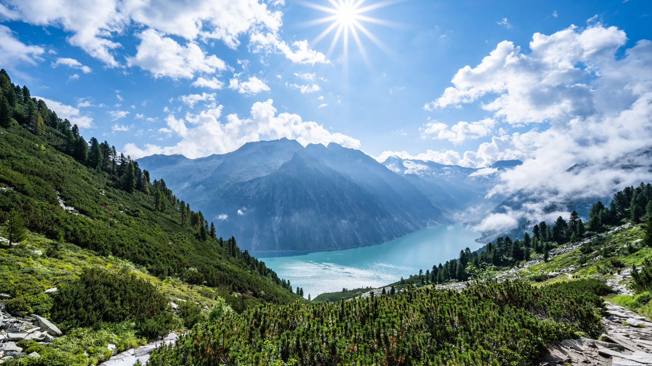 Scenic mountain landscape with a hiking path, turquoise lake, and bright sun on a summer day