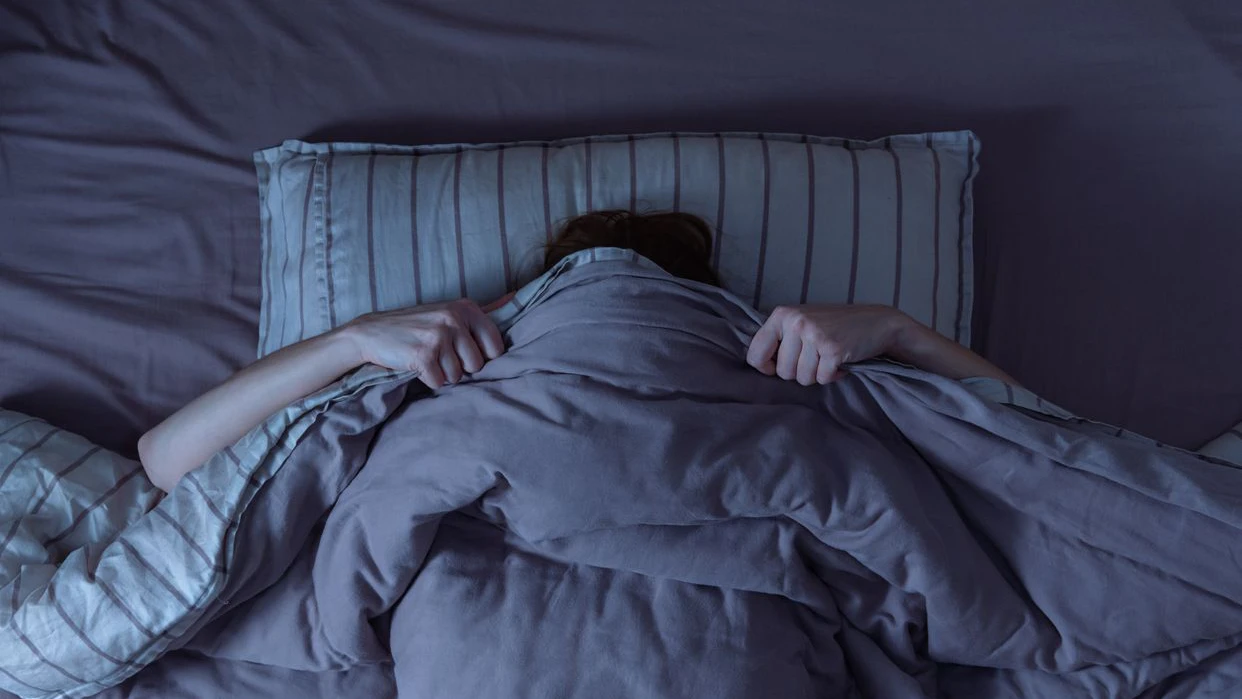 Top view of scared woman in bed covering her face with blanket.