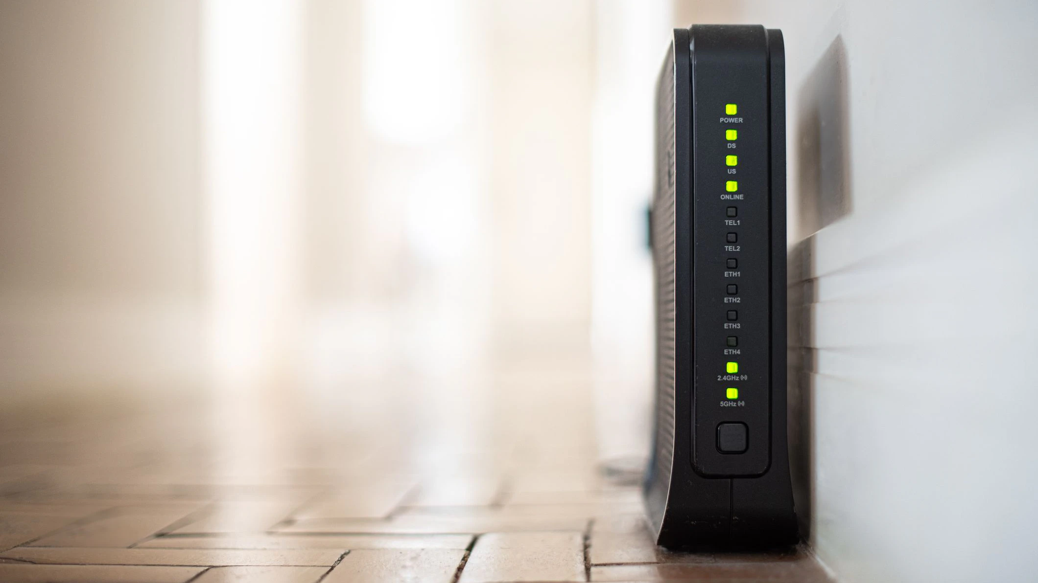Router - Wifi Modem, with flashing lights, on the floor, near the corner of a wall in a well-lit house.