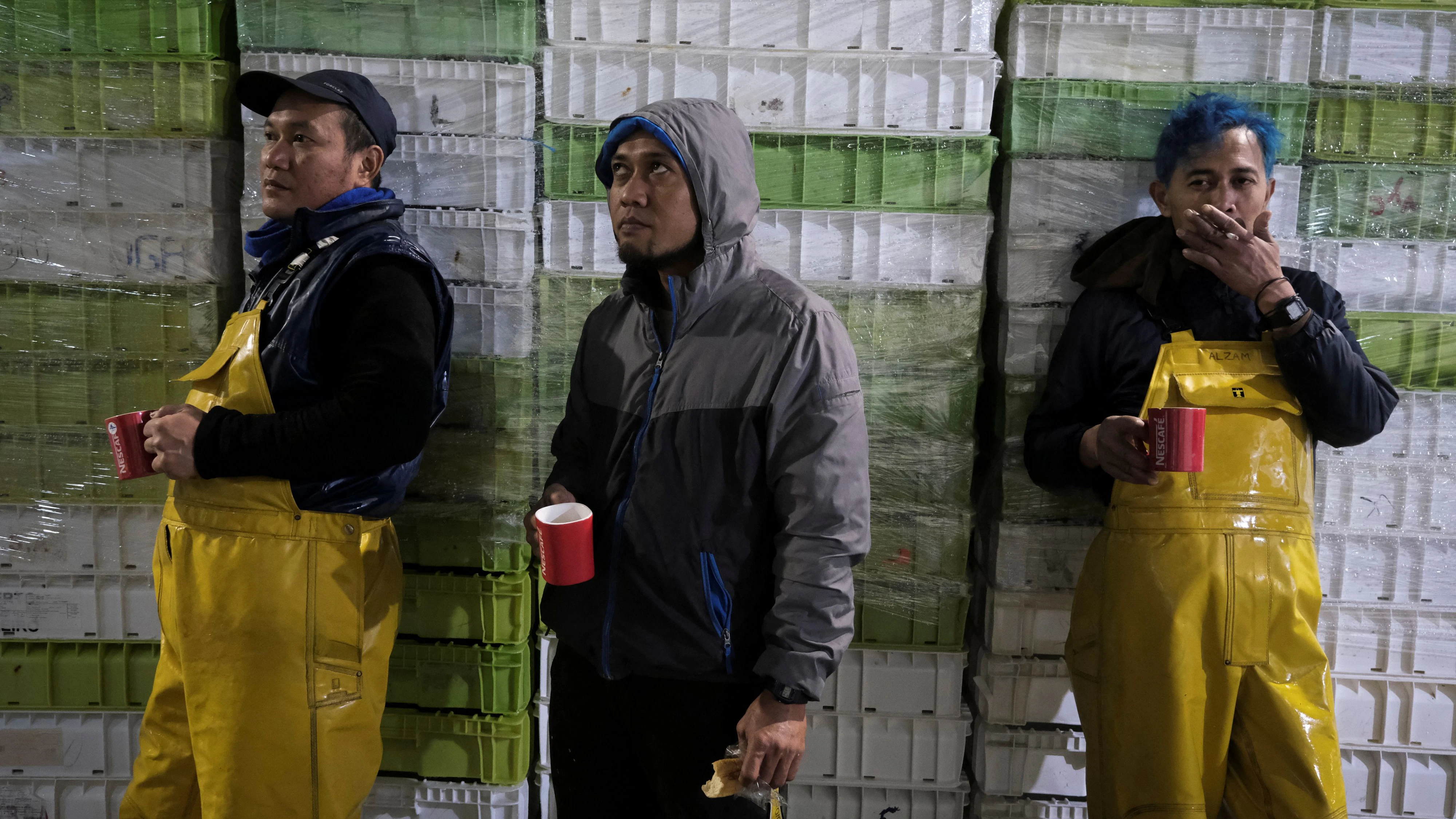Indonesian fishermen, Tobi (left), 43, Sujuh (center), 45, and Joe, 38, take a break after unloading the fish for an auction at Burela's port, Galicia, Spain, November 30, 2023. The fishing port of Burela has 44 nationalities among its 9,450 residents, including 90 men from Senegal and 244 from Cape Verde. Foreign workers make up about seven out of ten crew in Burela's fishing fleet, said Juan Carlos Otero of Burela's boat owners' association.       REUTERS/Nacho Doce      SEARCH "DOCE SPAIN MIGRANTS" FOR THIS STORY. SEARCH "WIDER IMAGE" FOR ALL STORIES.