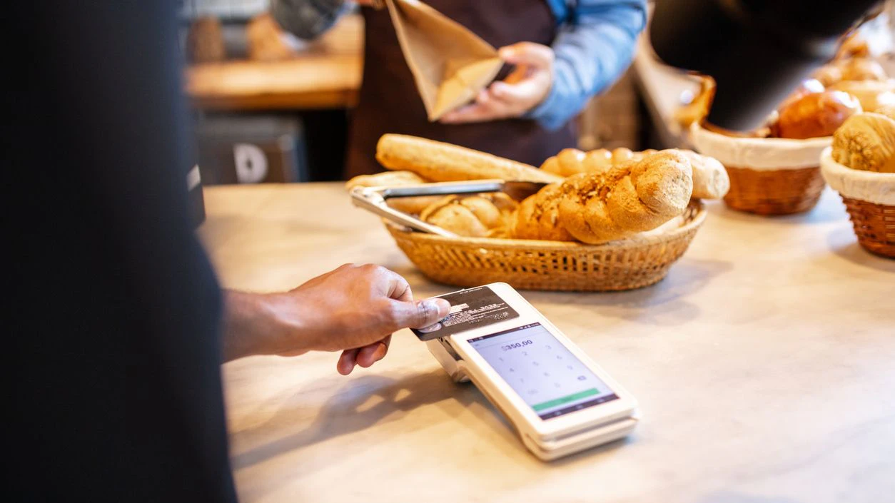 Closeup of a customer making contactless payment with credit card at bakery checkout counter. Customer buying food at a bakery.