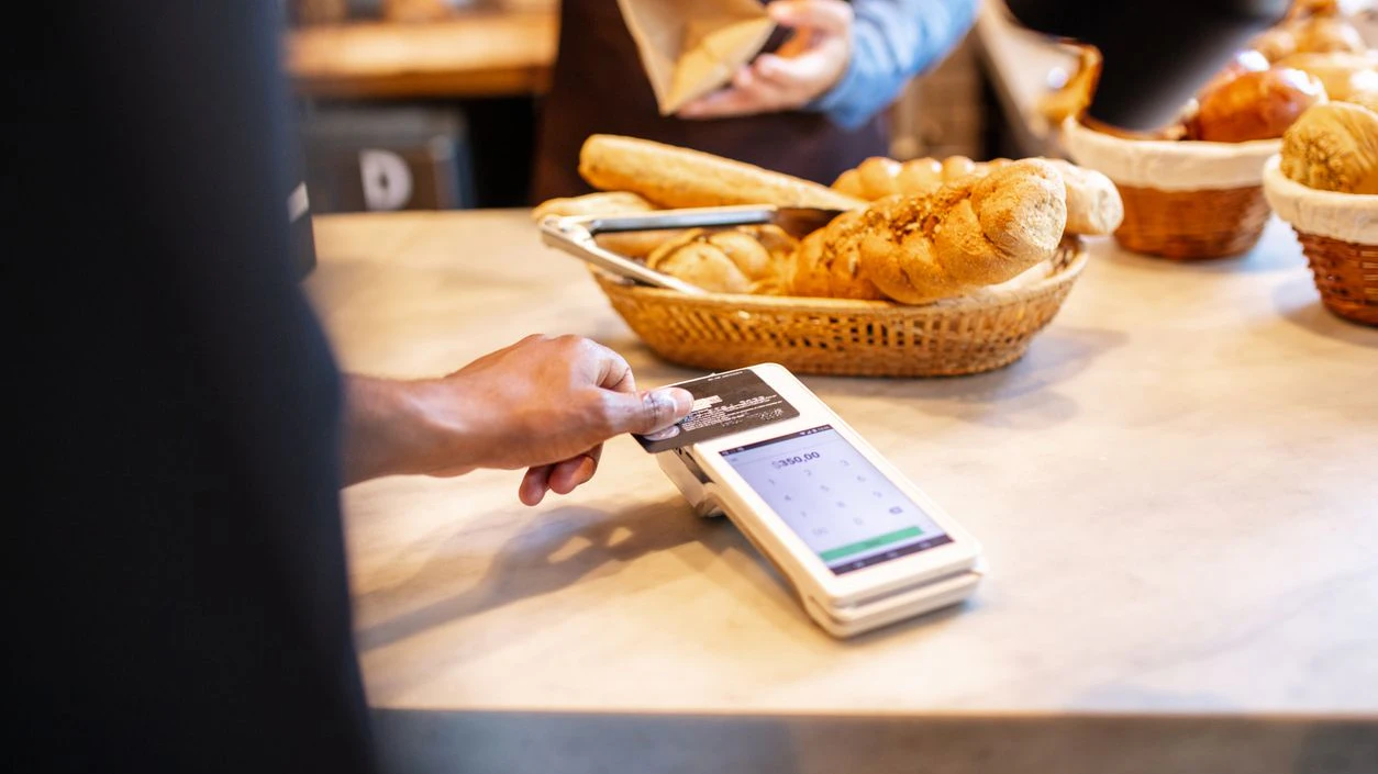 Closeup of a customer making contactless payment with credit card at bakery checkout counter. Customer buying food at a bakery.