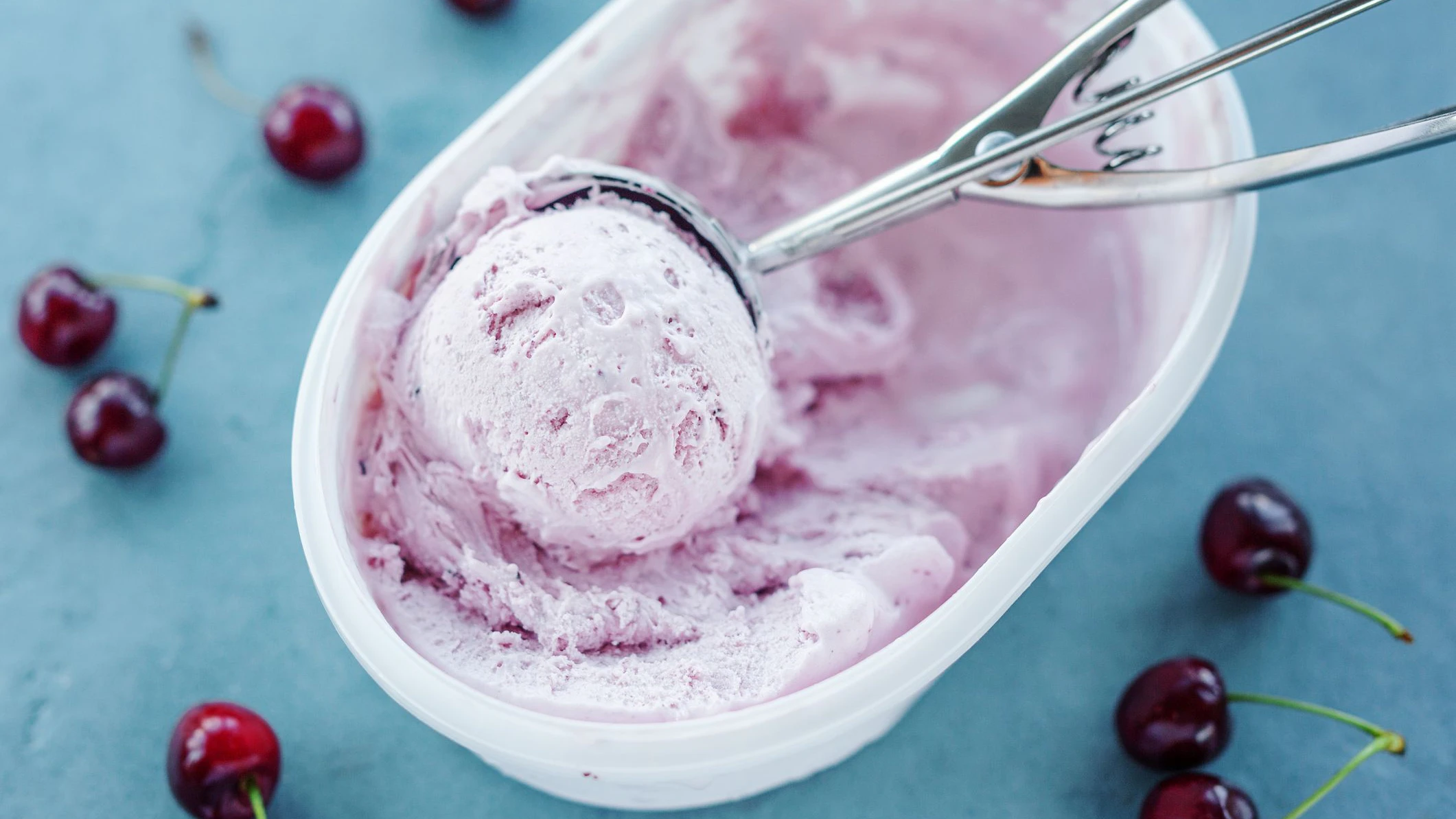 Tasty refreshing ice cream with cherry in plastic box on bright background.