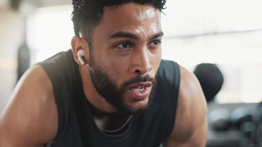 Man, sweating and tired in recovery for workout, intense exercise and wellness with fatigue. Male person, breathing and exhausted as athlete for health, challenge or training in fitness, sport or gym