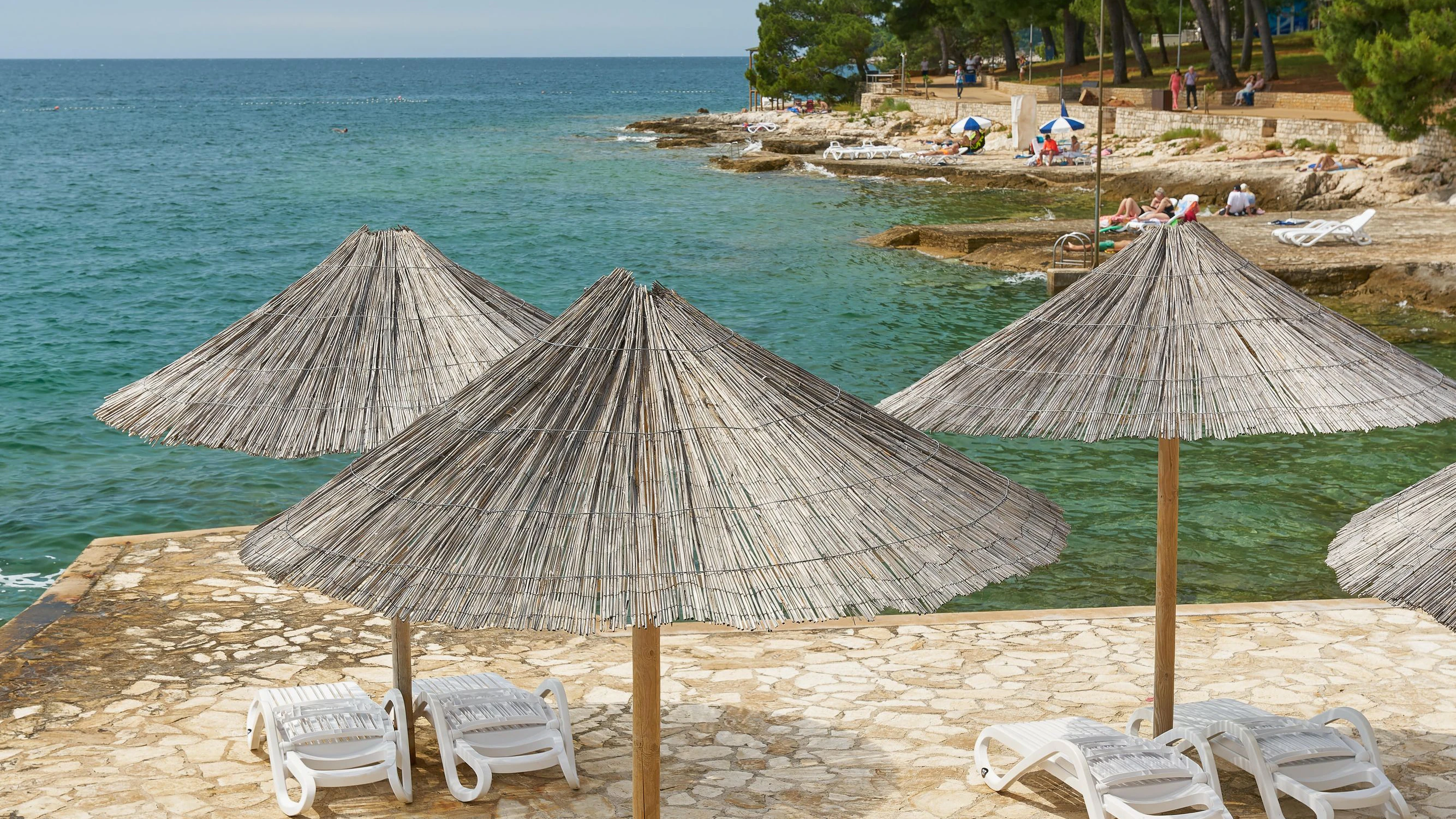 Sonnenschirm und Sonnenliegen an einer typischen Bdestelle am Strand von Porec an der kroatischen Küste der Adria