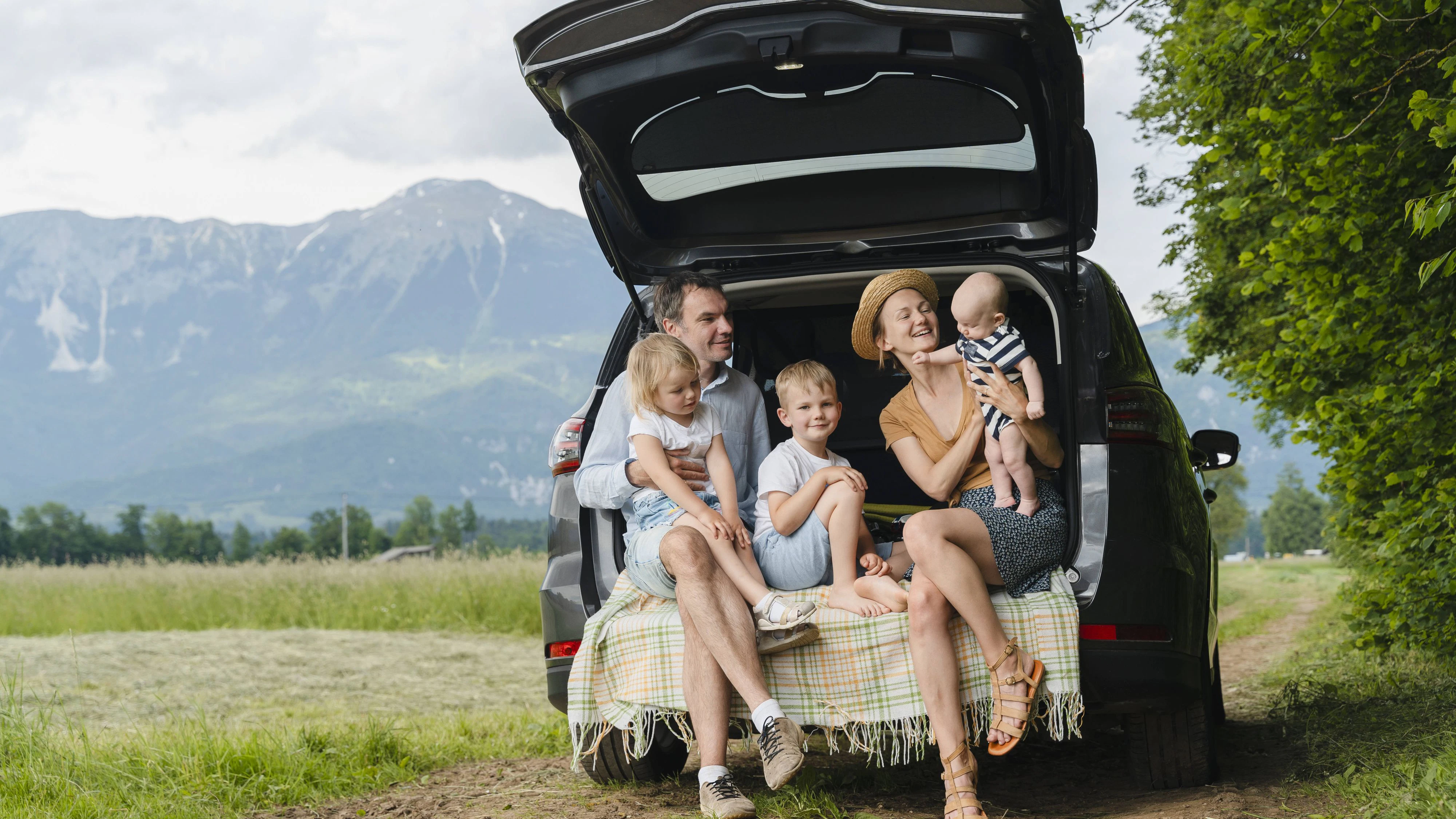 Family enjoying a summer road trip sitting on the open trunk of a car in nature model released, Symbolfoto, NDEF02221