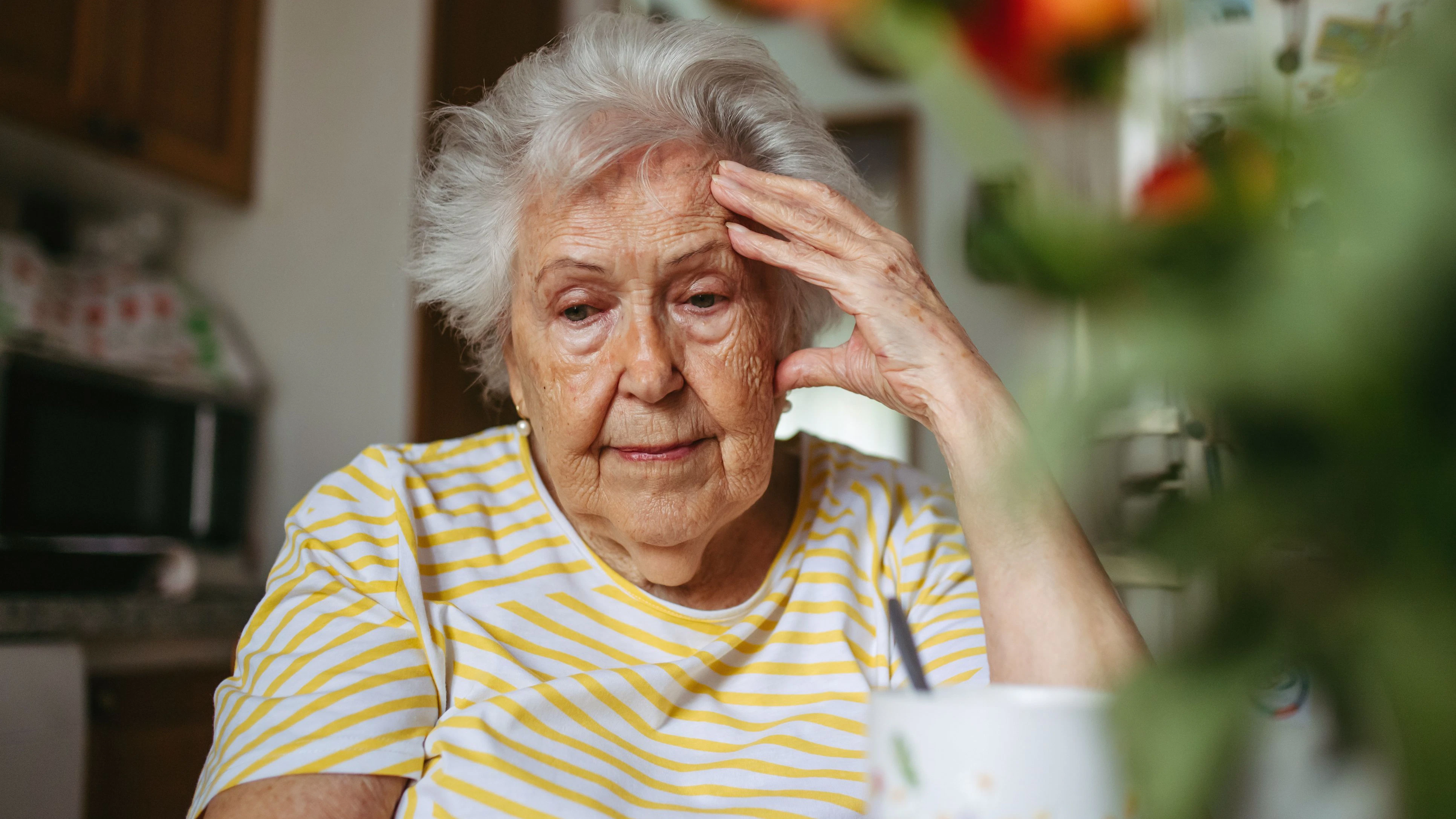 Portrait of worried senior woman crying in kitchen, covering face.
