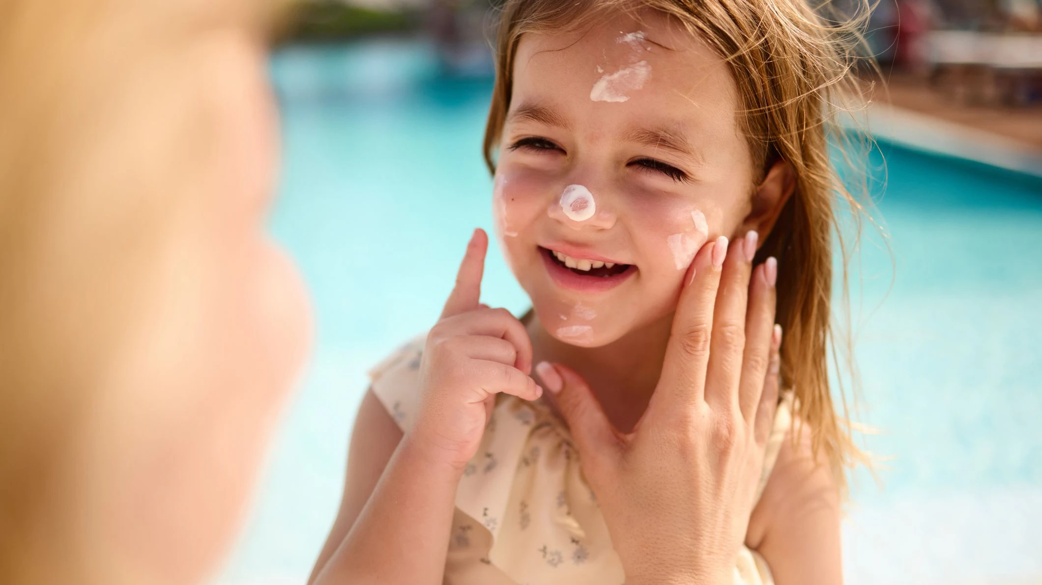 Happy girl enjoying while her single mother is applying moisturizer on her face during summer day.
