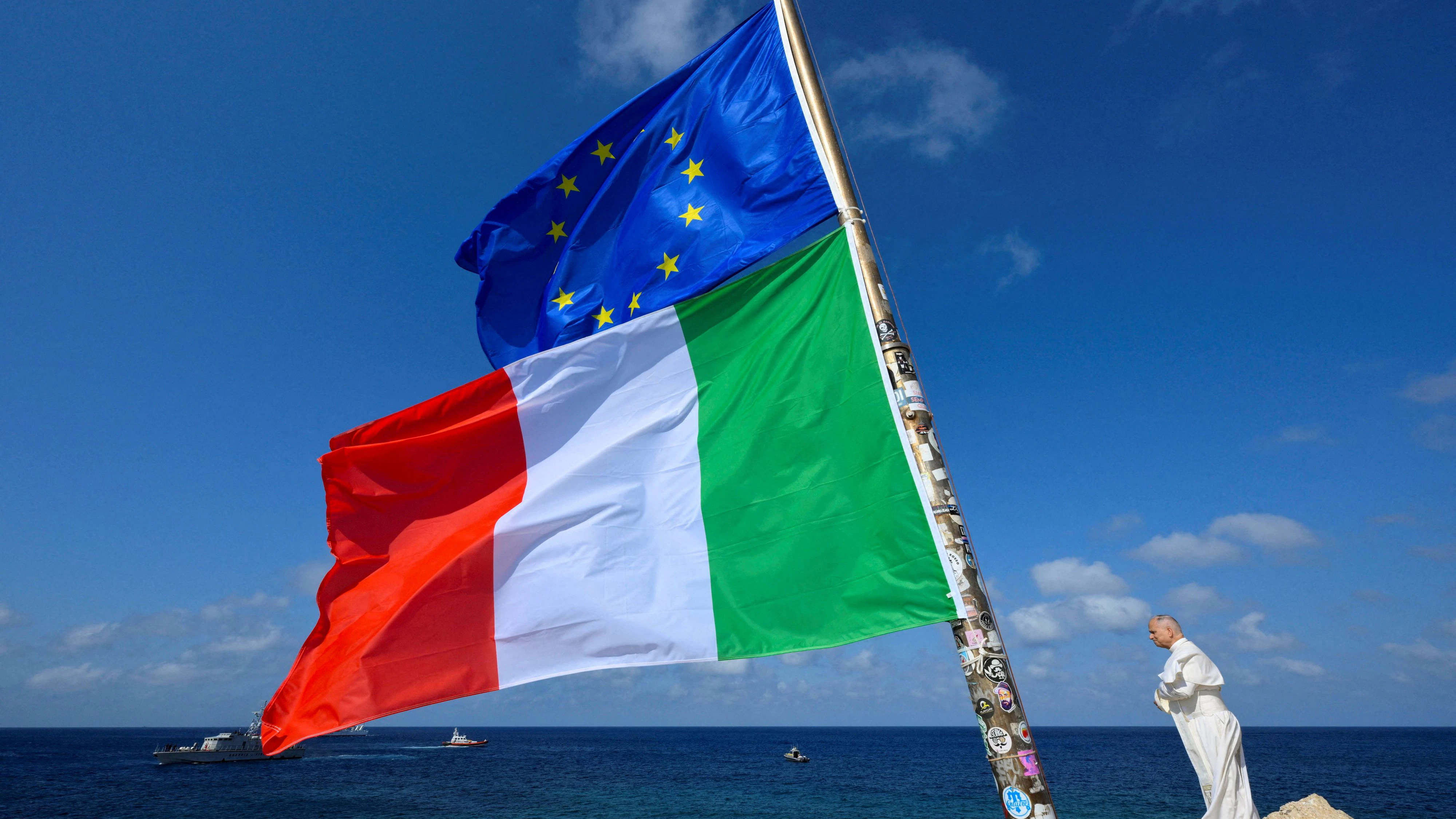 Pope Leo stands next to the European Union and Italy's flags  as he visits the island of Lampedusa, a key entry point for migrants crossing the Mediterranean Sea, during a pastoral trip, Italy, July 4, 2026.    Vatican Media/­Handout via REUTERS    ATTENTION EDITORS - THIS IMAGE WAS PROVIDED BY A THIRD PARTY.     TPX IMAGES OF THE DAY     