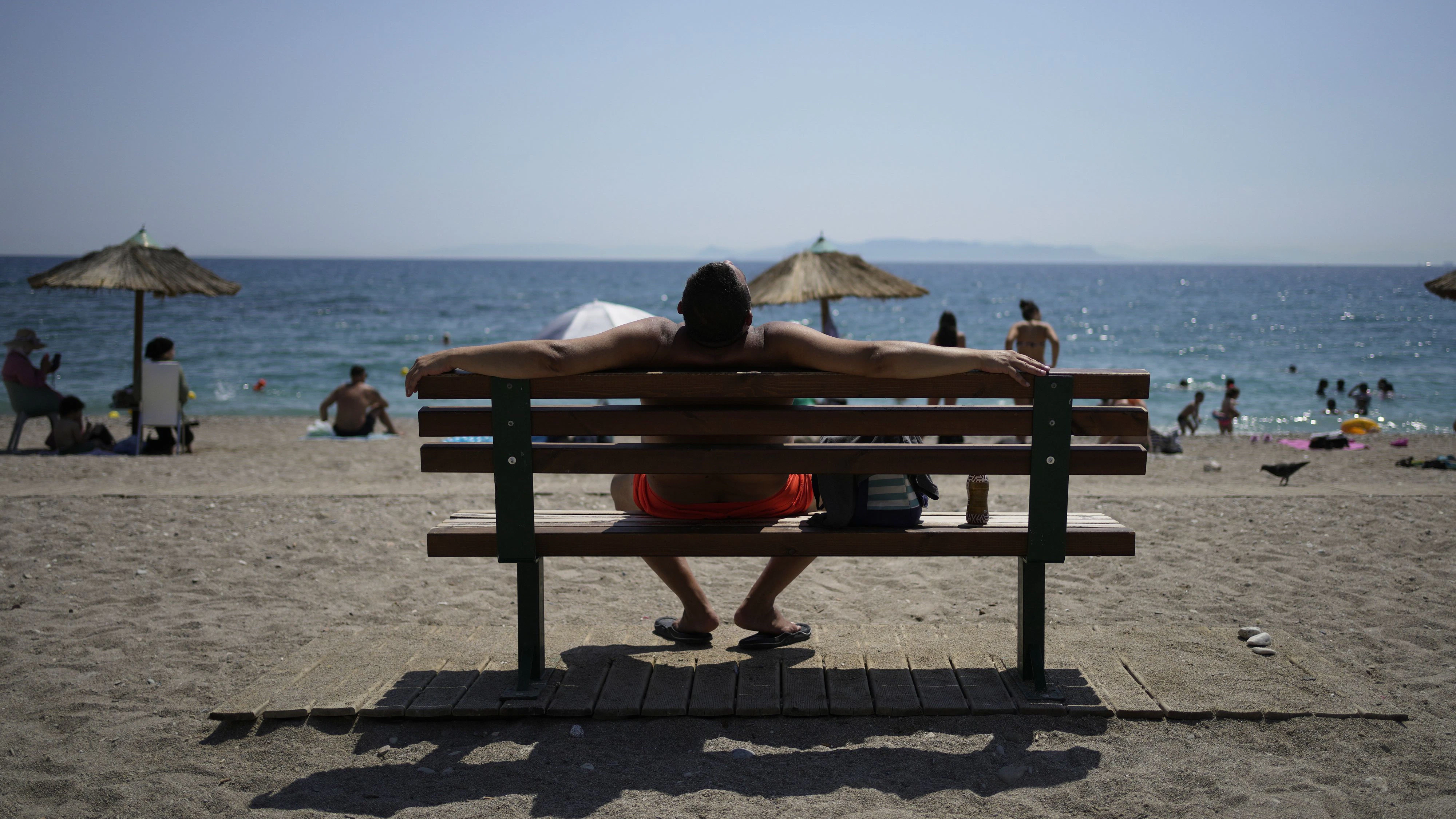 A man sunbathes sitting on a bench during a heatwave at the public beach of Paleo Faliro, in southern Athens, Greece, Monday, July 21, 2025. (AP Photo/Thanassis Stavrakis)