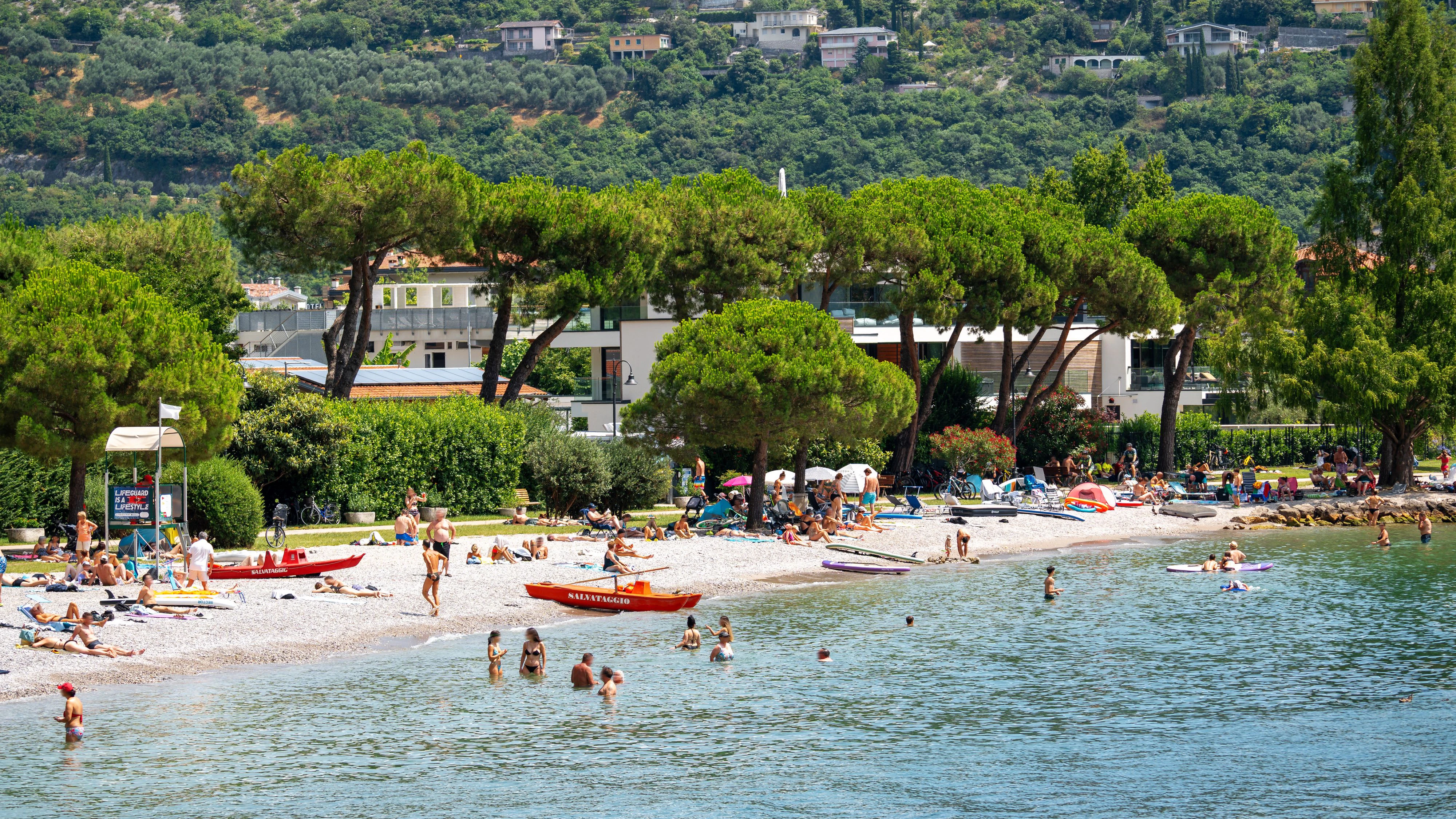 Ein belebter Strandabschnitt am Gardasee bei Riva del Garda und Torbole: Badegäste genießen Sonne, Wasser und Erholung, während das Rettungsboot für Sicherheit sorgt - Sommerfeeling pur in Norditalien.