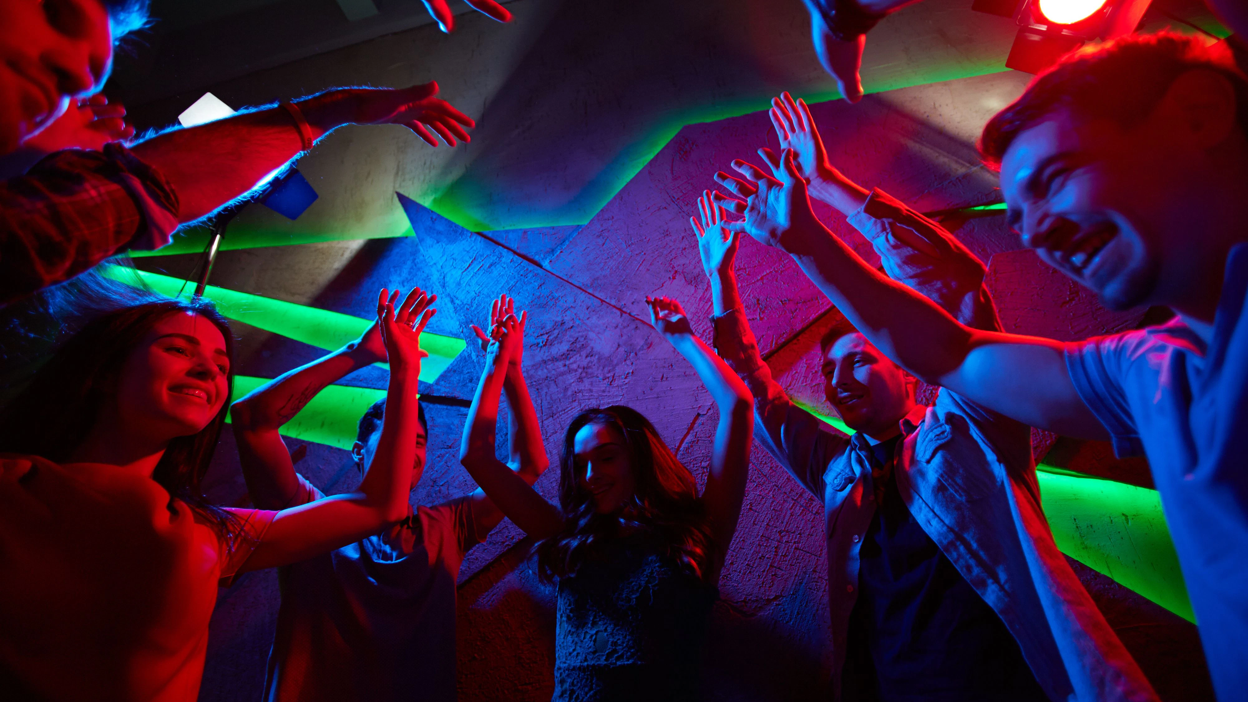 Guys and girls raising hands during energetic dance in night club
