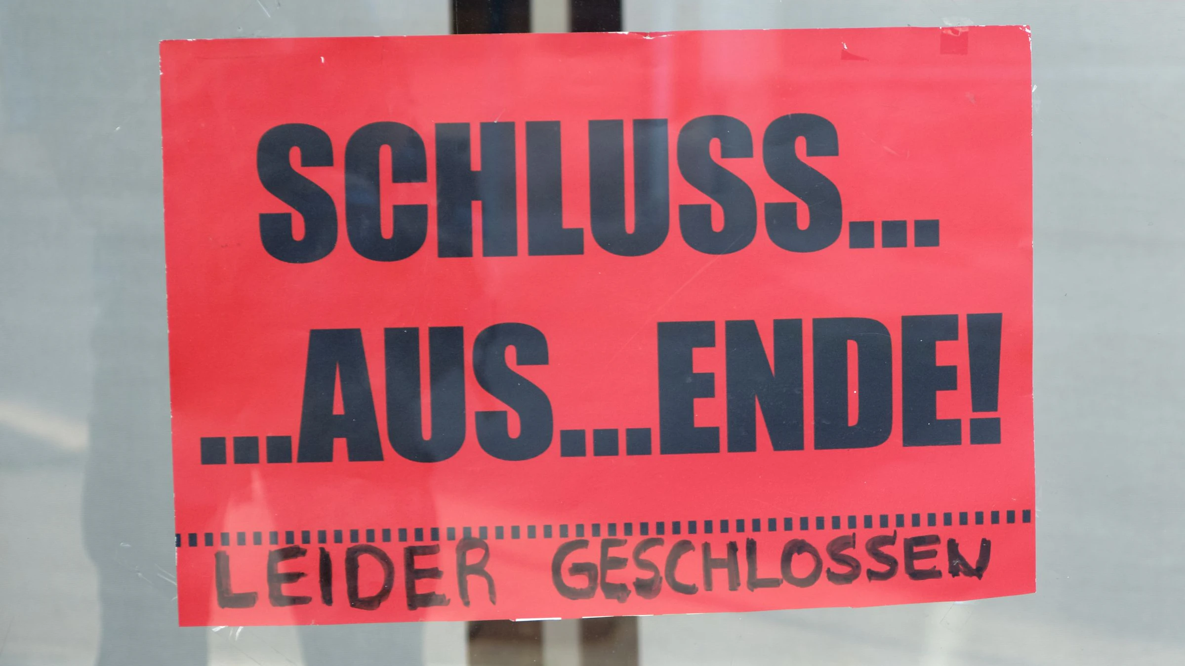 A red sign on the glass doors of a closed department store says "Schluss.... Aus.... Ende! Leider geschlossen" because of the business closing down.