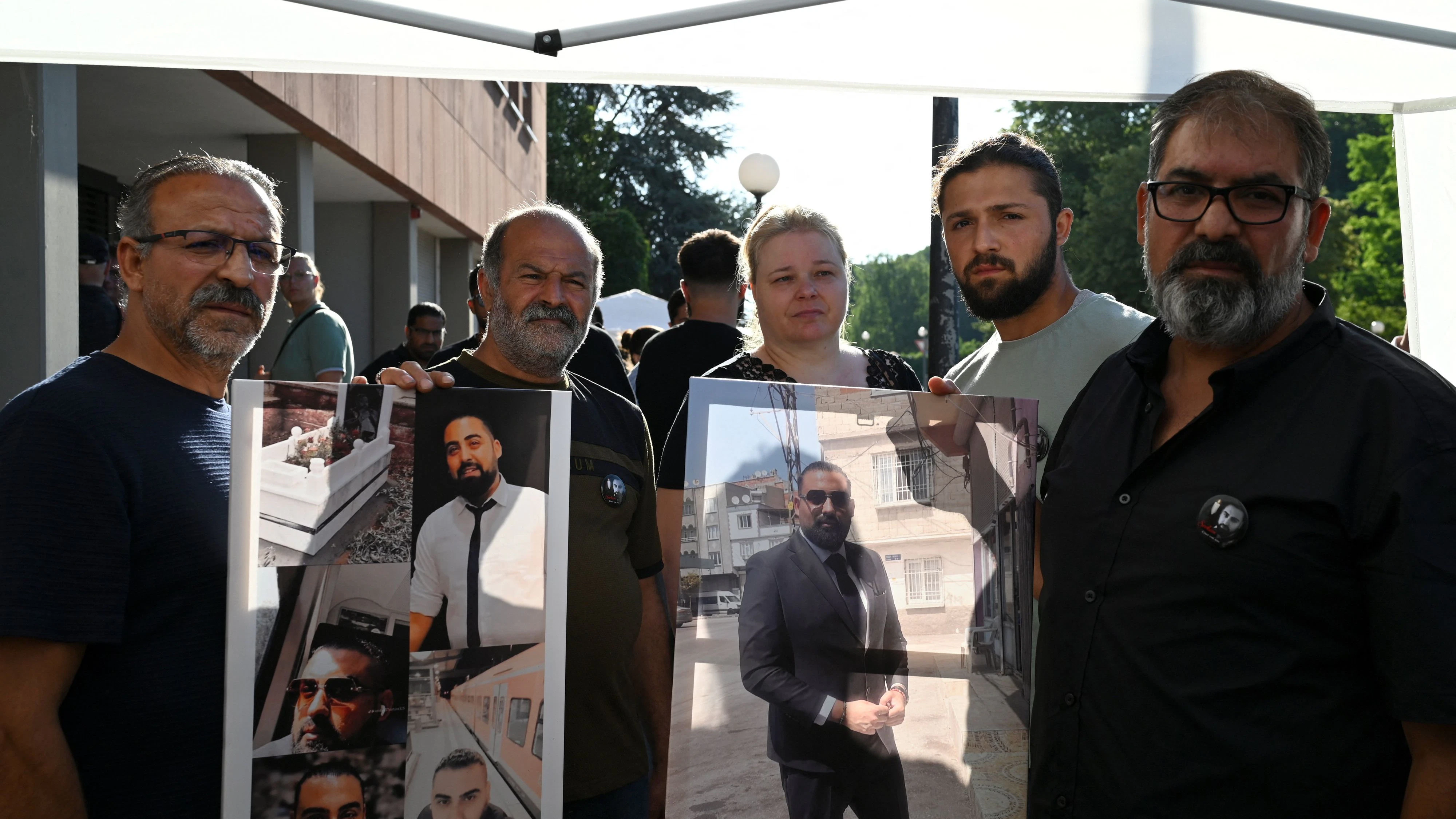 Erdal C., der Vater des getöteten Zugbegleiters Serkan C., und weitere Familienangehörige halten Fotos des Verstorbenen in den Händen. 