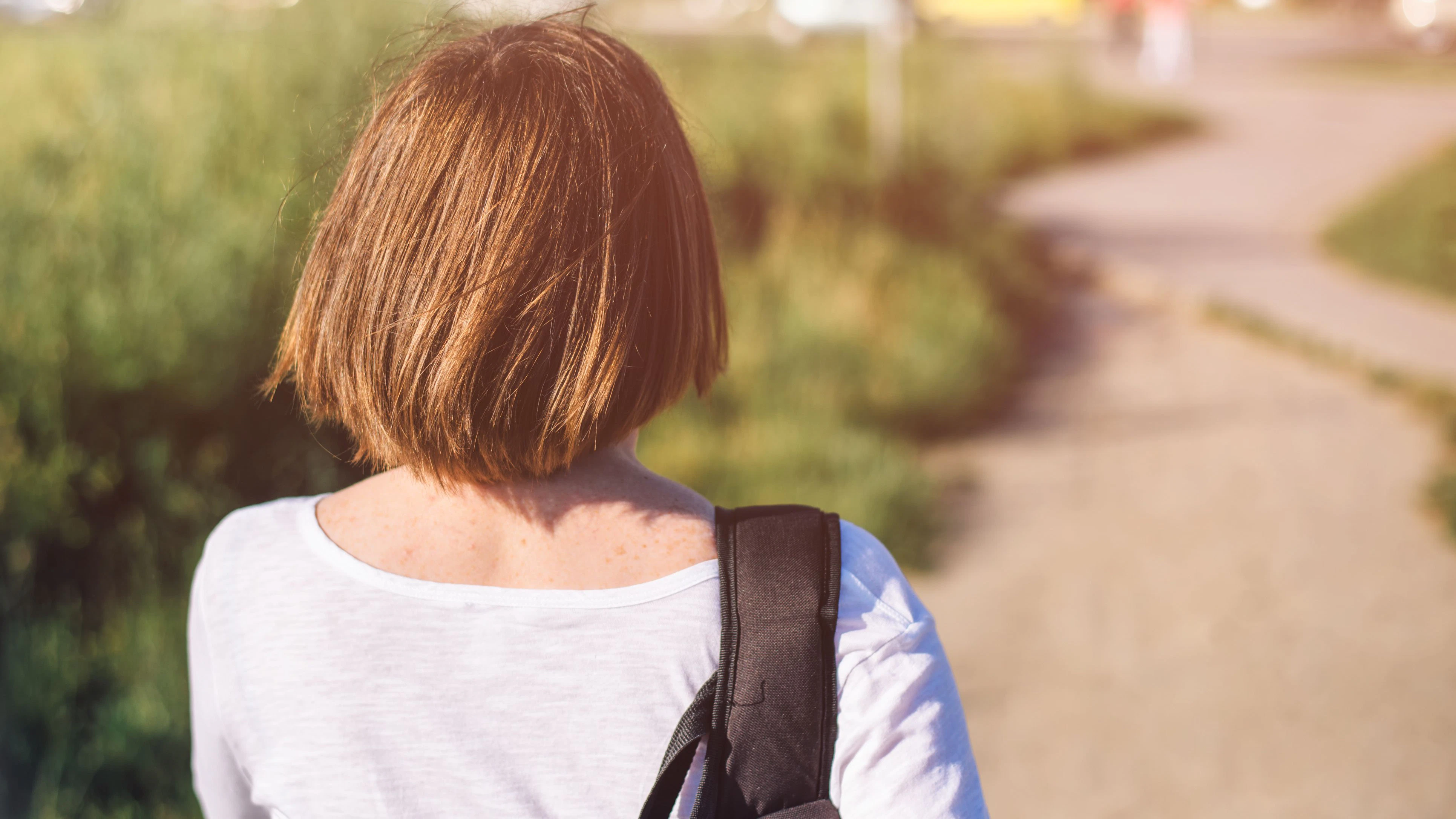 Casual ordinary young adult woman in everyday activity walking on city streets, from behind, selective focus