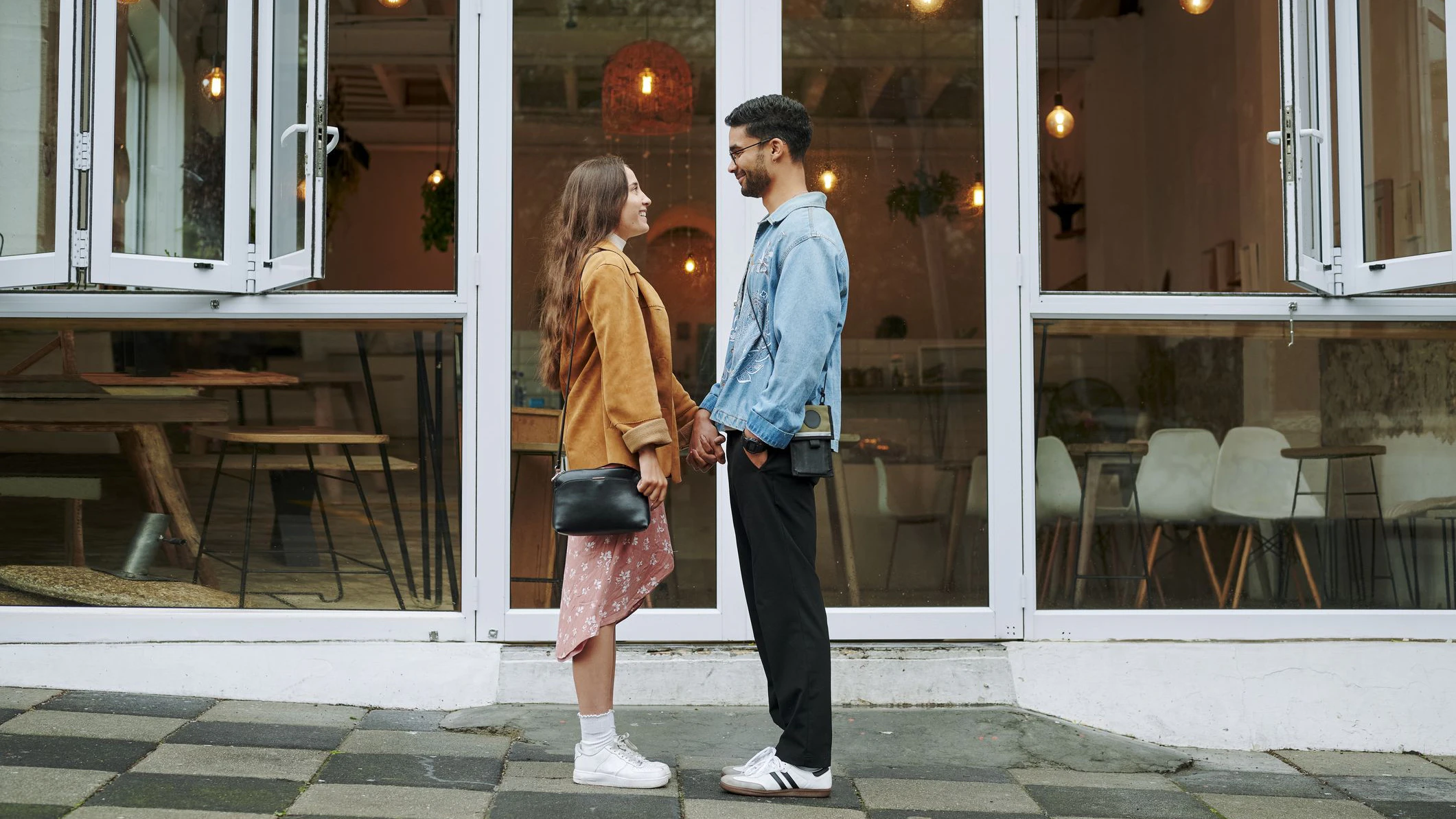 Smiling young couple holding hands together and standing face to face on a sidewalk outside of a cafe
