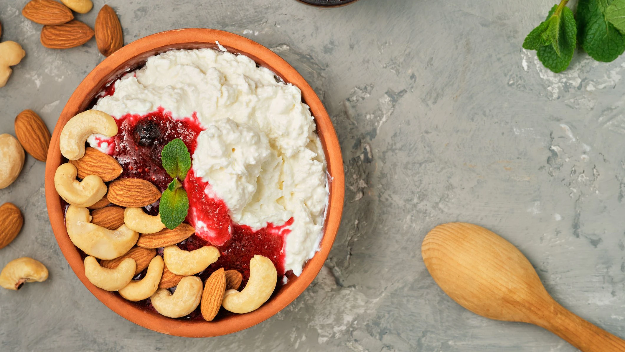 Fresh cottage cheese with sour cream, cranberry jam and nuts in traditional clay bowl. Neutral gray background. Healthy breakfast made from curd, top view with copy space