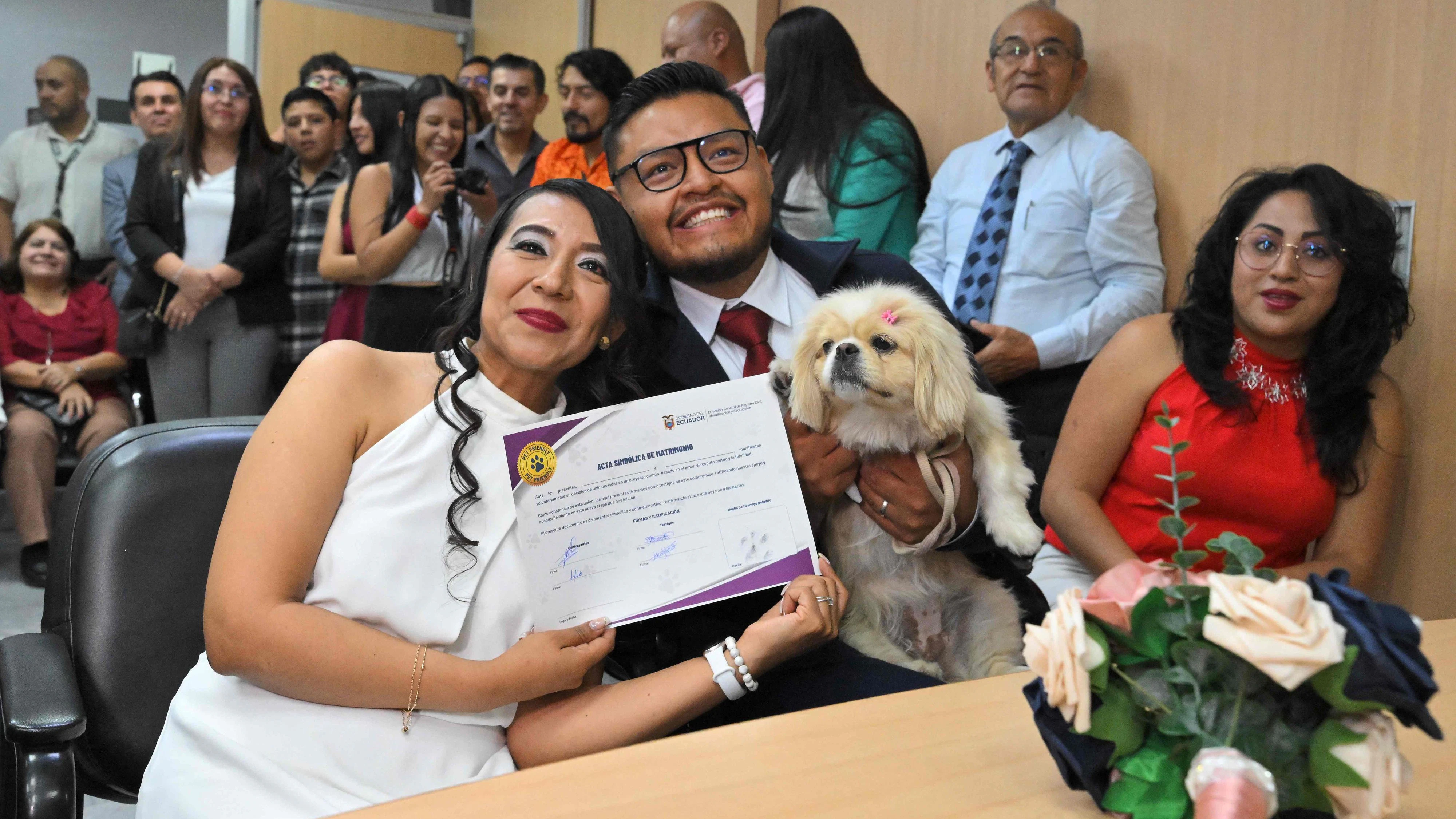 Andres Alquiga and Diana Tupiza with their pet Luna, show the symbolic marriage certificate with their pet's "signature" after their wedding at the central civil registry office in Quito on July 7, 2026. With the regulation of "pet-friendly" marriages, the Andean country took a step ahead of the rest of Latin America, where in most nations the only witnesses allowed are humans. In Argentina and Mexico, there have been exceptional cases due to specific decisions by the authorities. (Photo by Rodrigo BUENDIA / AFP)