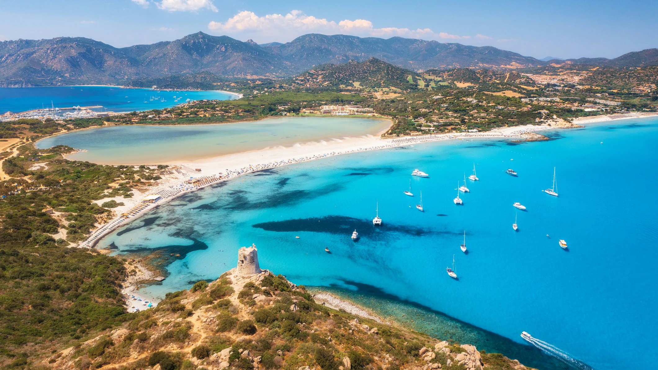 Aerial view of beautiful sandy beach, old tower on the hill, sea bays, mountains at summer sunny day. Porto Giunco in Sardinia, Italy. Top view of blue sea with clear water, white sand, mountains