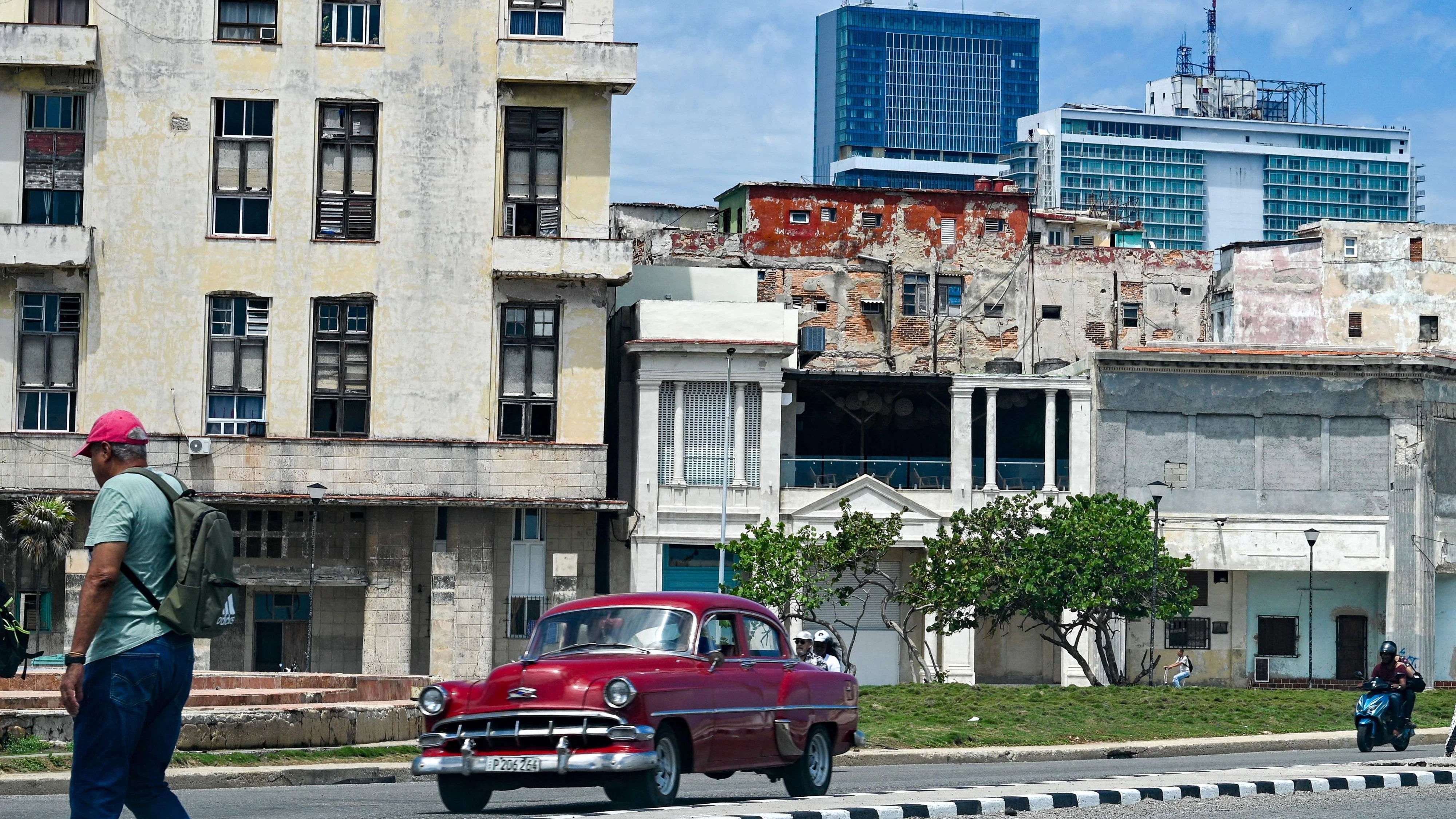 A man walks along a street as a classic car drives past, with the Iberostar Selection hotel (C) and the Habana Libre Melia hotel (R) in the background in Havana, on June 2, 2026. The Spanish hotel group Iberostar has withdrawn from managing around a dozen hotels in Cuba that it operated in partnership with the military-linked conglomerate Gaesa, which is under US sanctions, several sources close to the matter told AFP on June 2, 2026. (Photo by ADALBERTO ROQUE / AFP)