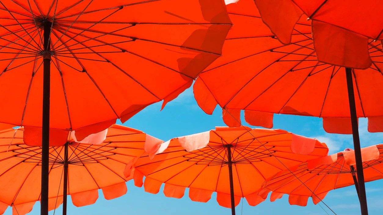 Low angle view of vibrant red and orange beach umbrellas with clear blue sky in background on sunny summer day. Relaxation, vacation, holiday background concept