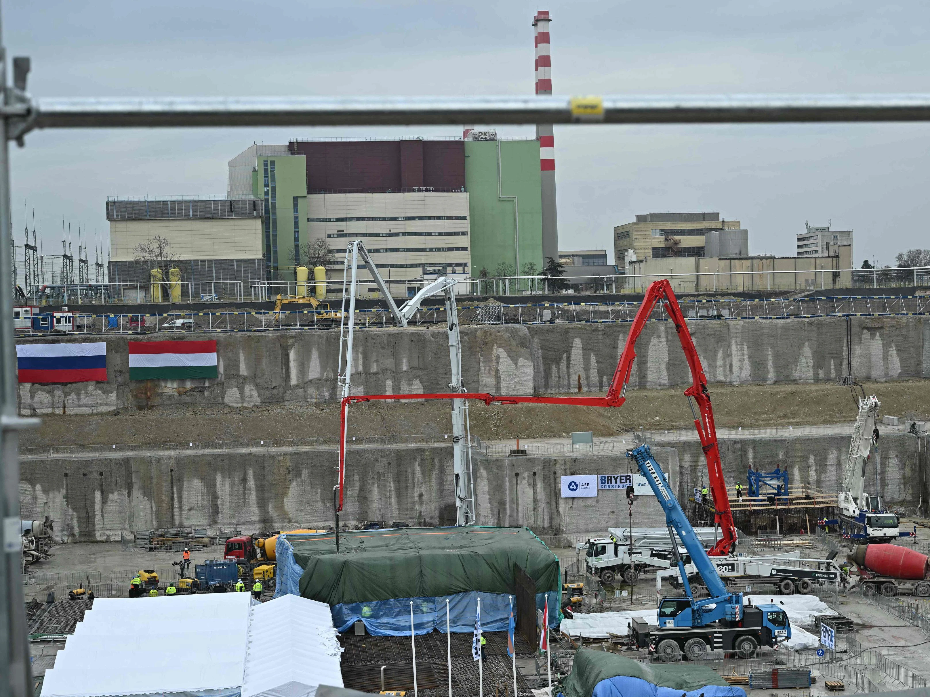 Ein Überblick zeigt die ungarische (rechts) und die russische (links) Nationalflagge an einer Wand sowie Arbeiter und Fahrzeuge auf dem Paks-II-Gelände im Süden Ungarns. Im Februar 2026 wurden die Betonarbeiten für die Fundamentplatte des ersten Technikgebäudes begonnen.