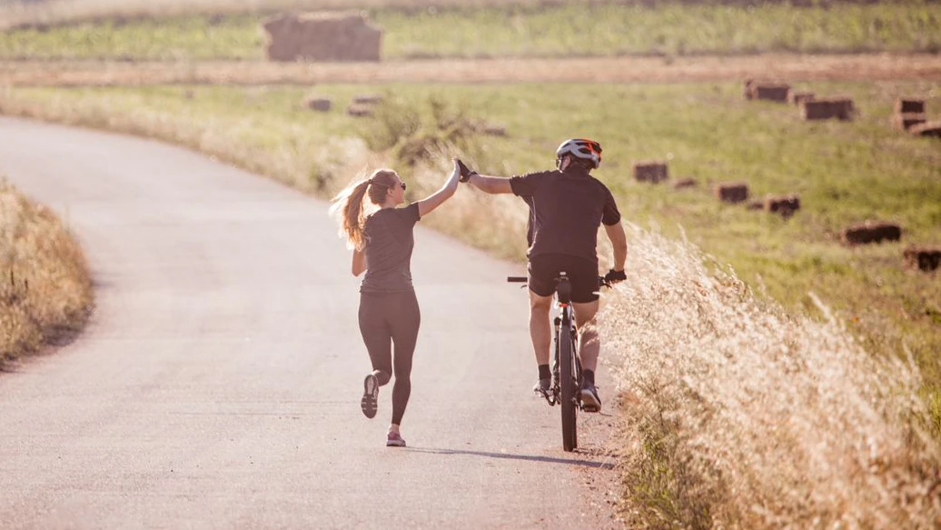 Man is riding a bike and woman is running next to him on the empty road in the coutryside