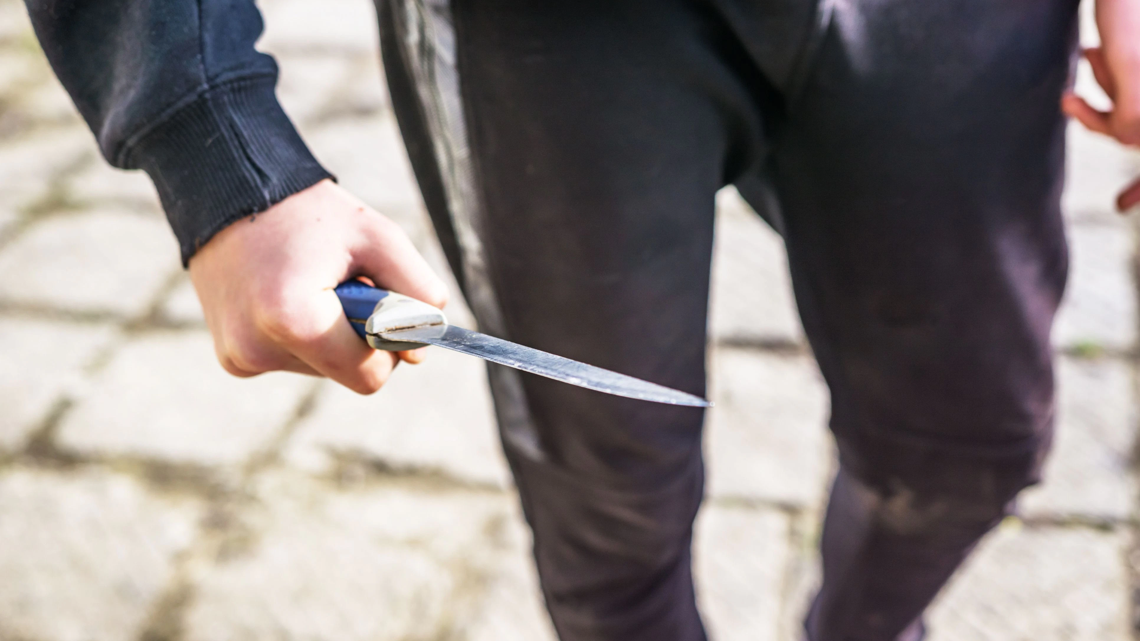 Close-up of a young man's hand with a knife, a big blade. Arrogance and violence among young people. Shallow depth of focus.