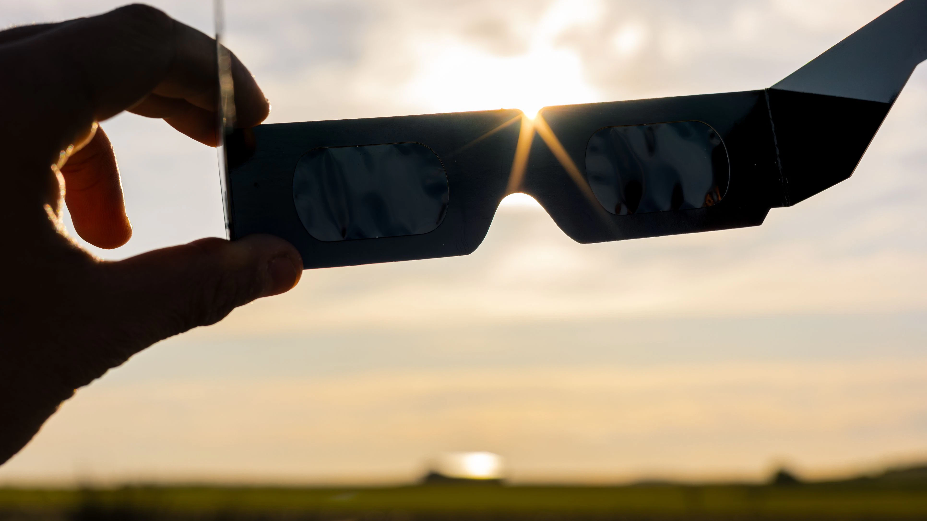 Person holding solar eclipse glasses, gazing up at the dazzling sun to safeguard their eyes during a rare celestial occurrence