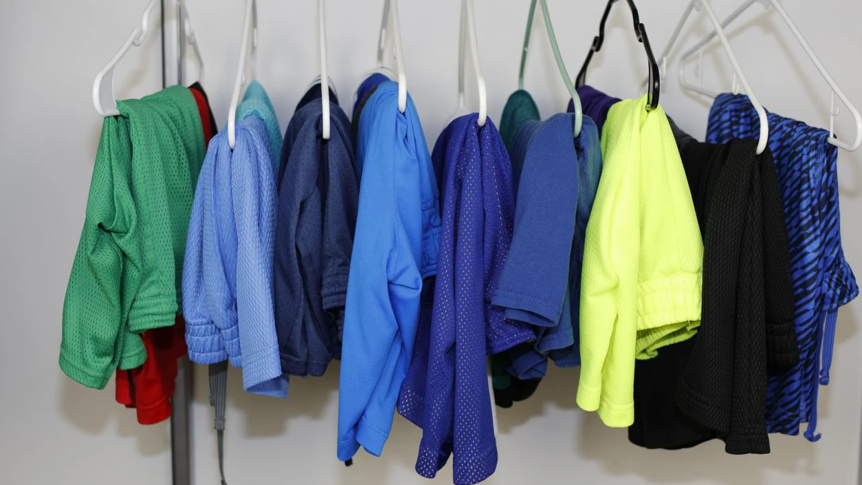 Many different colors of men’s gym shorts and sport shorts hanging on hangers in a closet closeup. A variety of different color sport shorts mostly with pockets used for exercising hanging in a closet