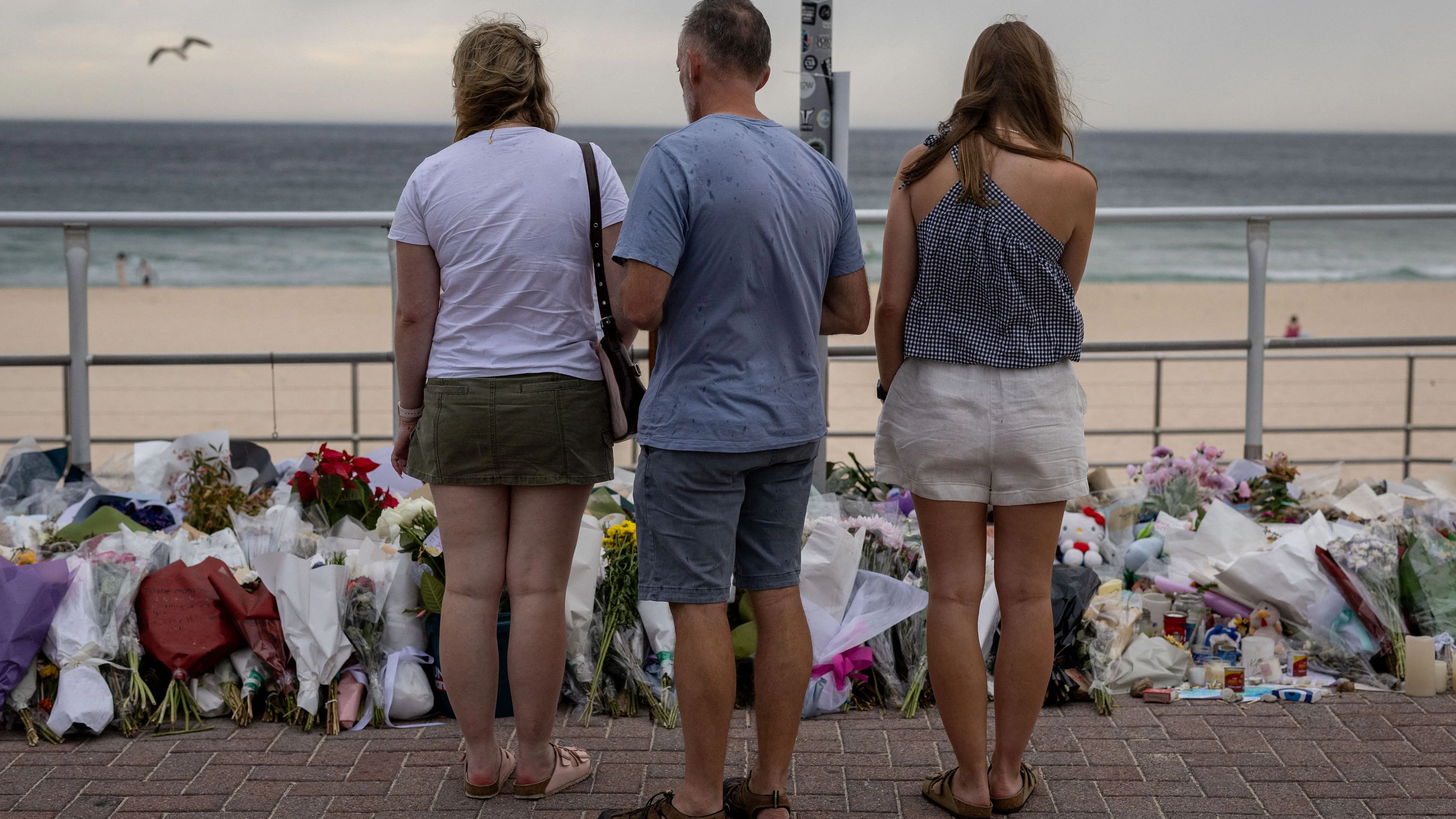 People stand in front of flowers offered to honour the victims of a mass shooting during a Jewish Hanukkah celebration at Bondi Beach on December 14, in Sydney, Australia, December 19, 2025. REUTERS/Eloisa Lopez 