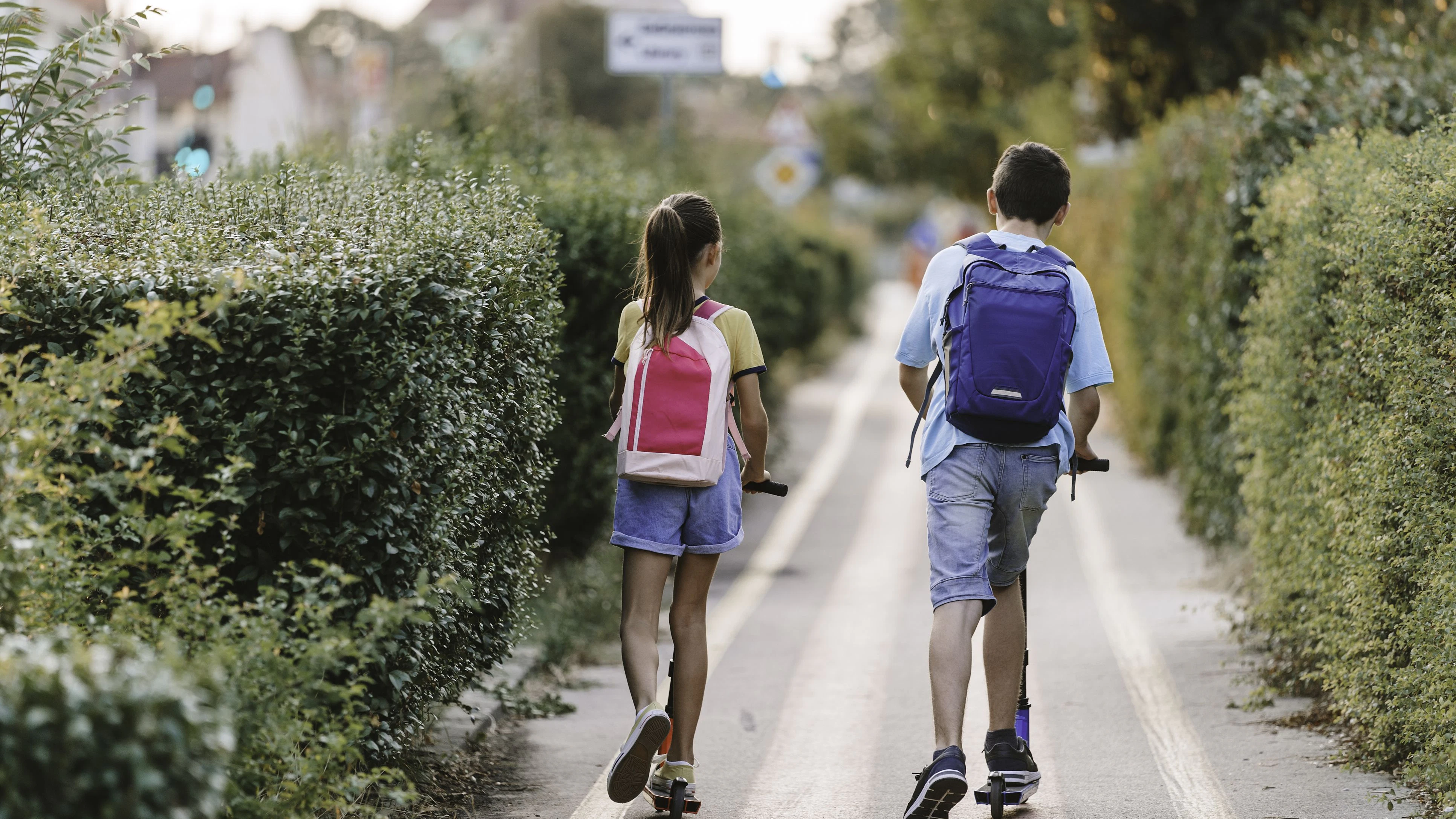 Brother and sister riding with scooter in the city with backpack. Two kids biking on way to school. Copy space.