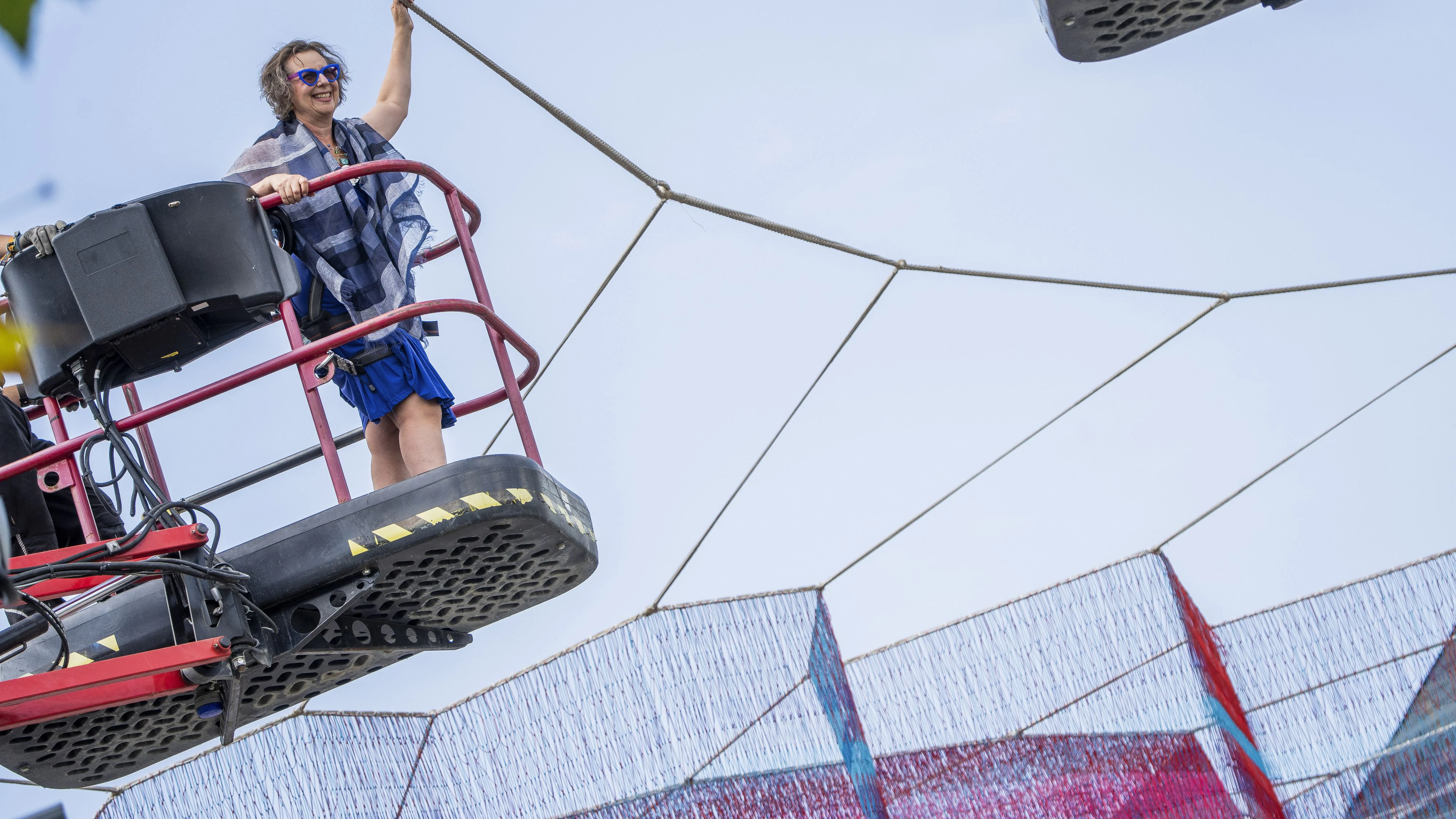 Die Künstlerin Janet Echelman steht auf einer Hebebühne über ihrer Netzskulptur „A Sky Full of Hope – Earthtime 1.78 Frankfurt“, die über der Konstablerwache schwebt.