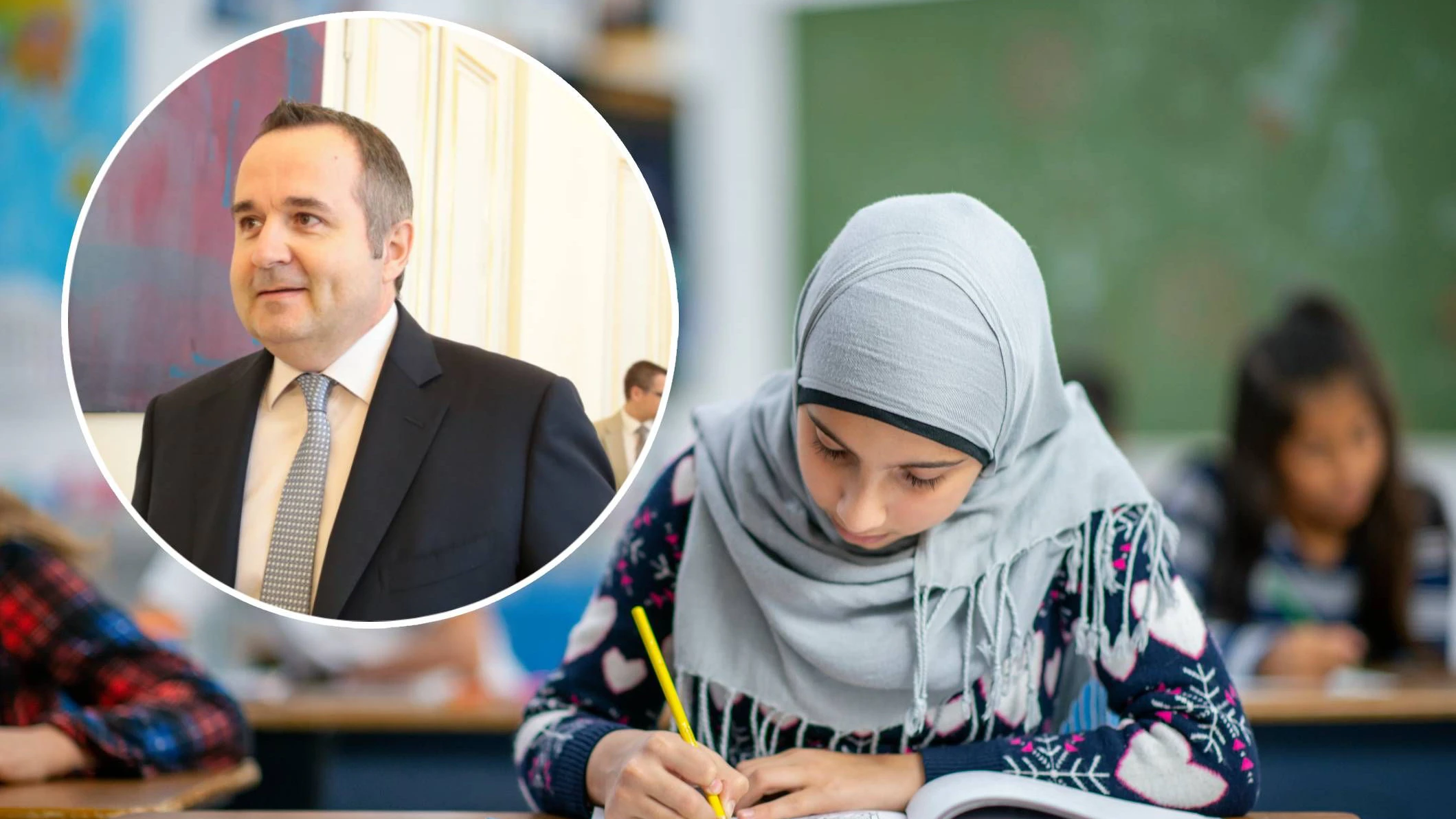 An Afghan elementary student sits at her desk among her multi-ethnic peers writing in a book at her desk.  She is looking down at her desk and focused on the task.  She is wearing a head scarf and is dressed casually.