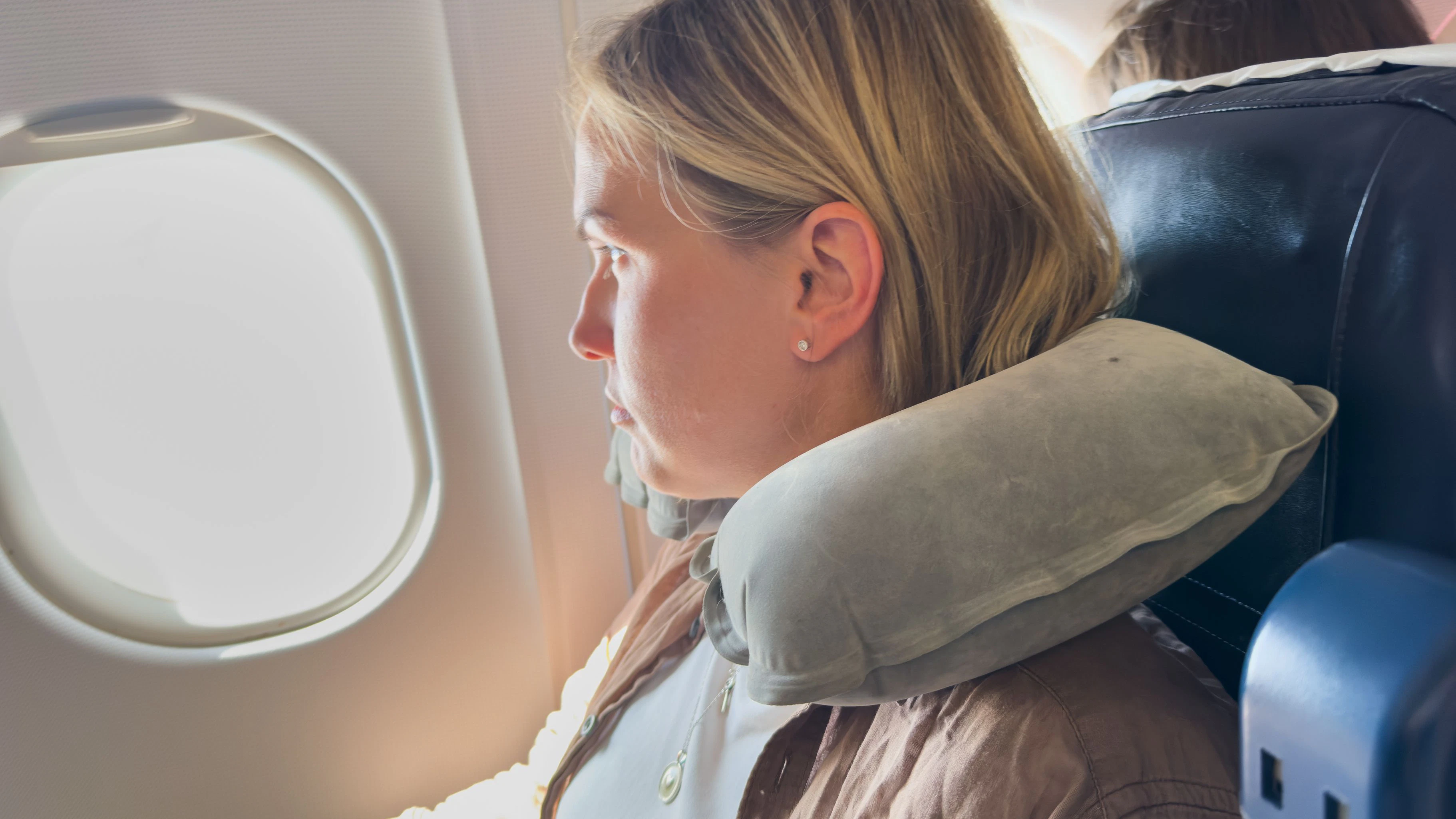 Passenger woman is flying in plane. Girl sitting in airplane looking out window going on trip vacation travel. Traveling female inside plane enjoying flight. Traveling girl