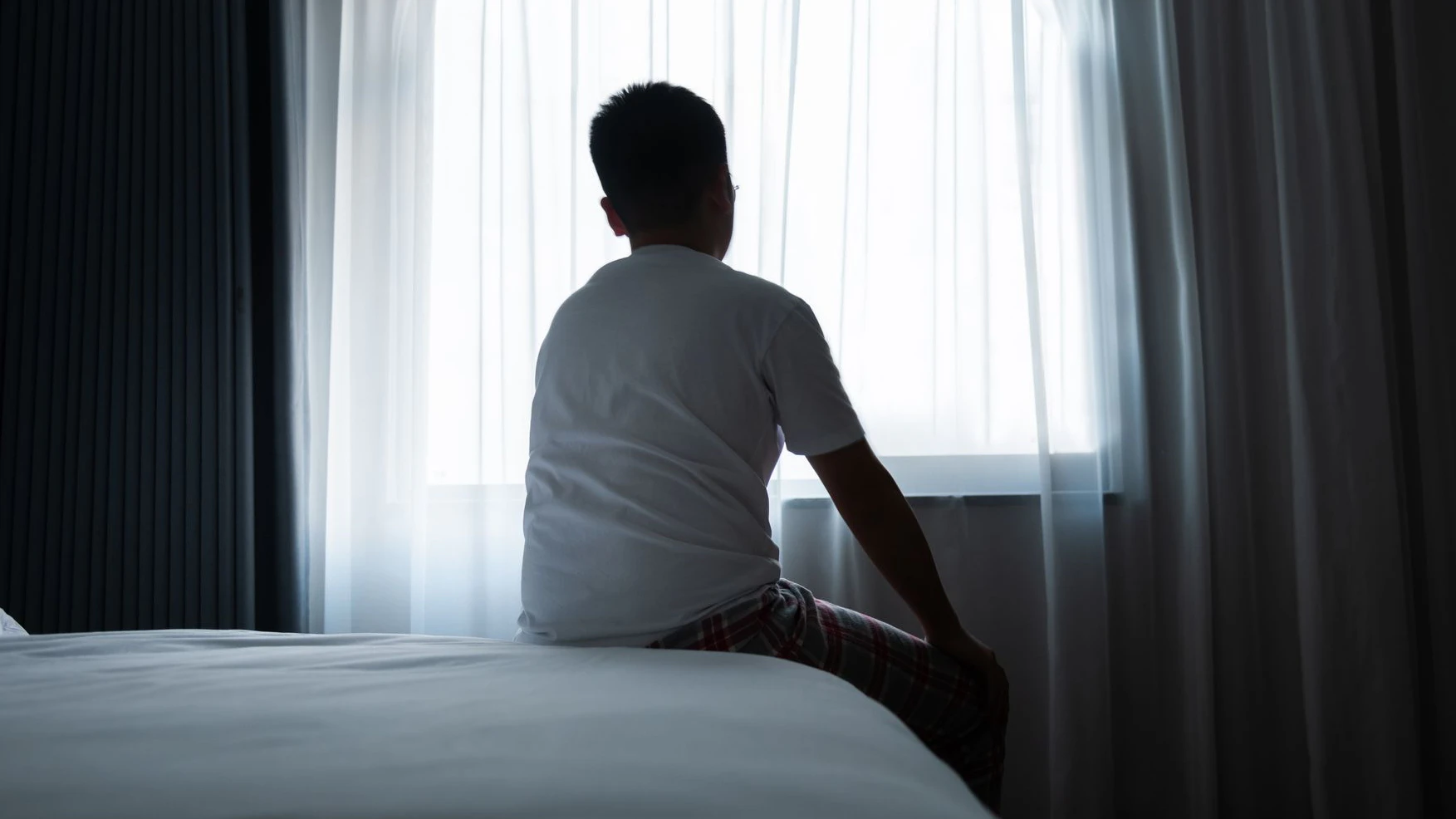Rear view of a teenager boy sitting on bed