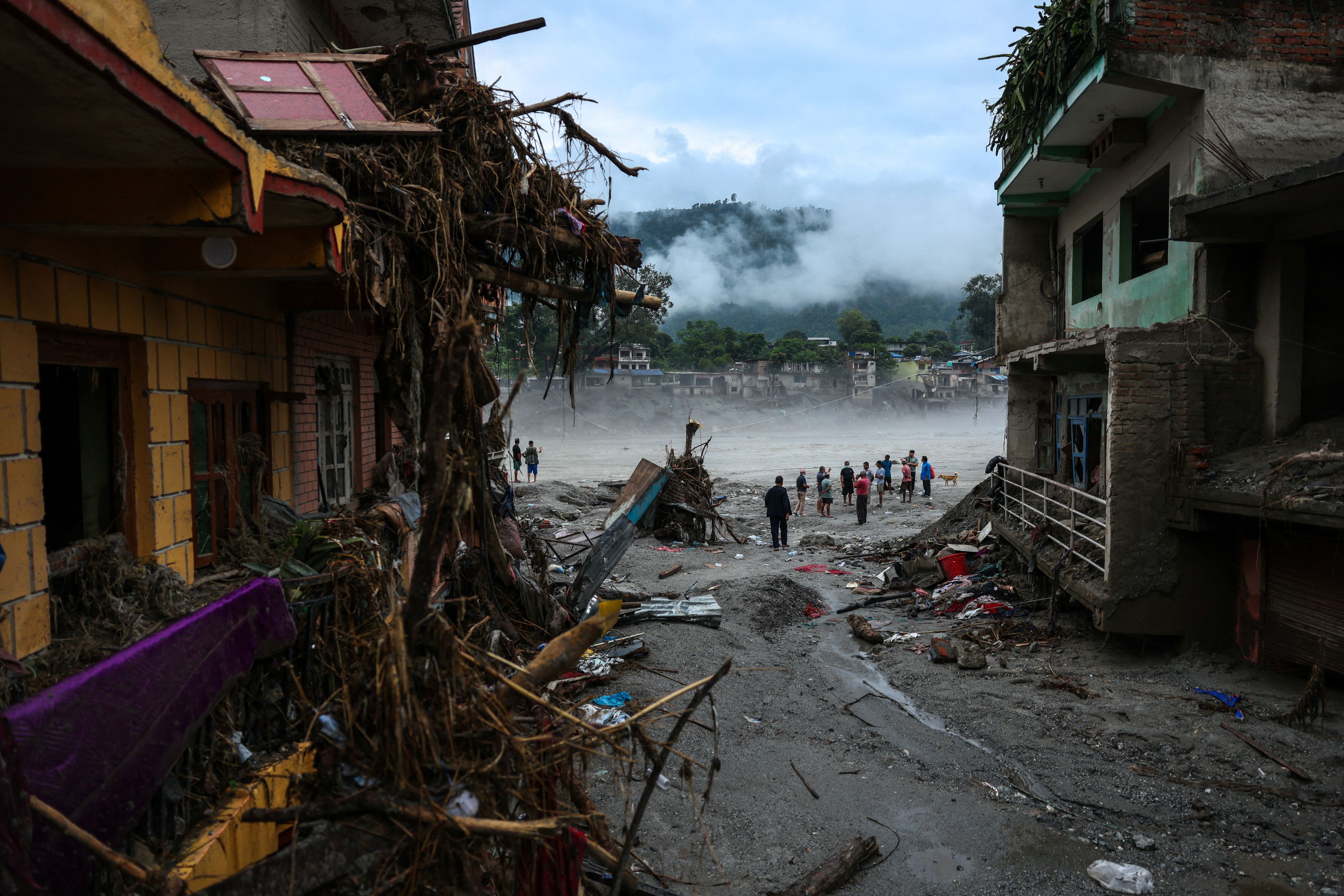 Menschen stehen neben beschädigten Gebäuden nach den verheerenden Sturzfluten und einem Schlammlawinenunglück in Devighat im Distrikt Nuwakot, Nepal, am 4. September 2026.