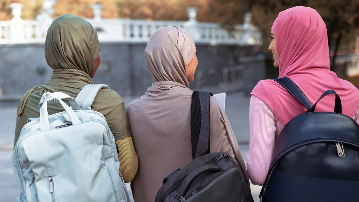 Three Unrecognizable Muslim Students Ladies With Backpacks Walking Back To Camera In Park Outdoor. University Education And Lifestyle, Study And Degree For Modern Arab Female Women Concept. Rear View