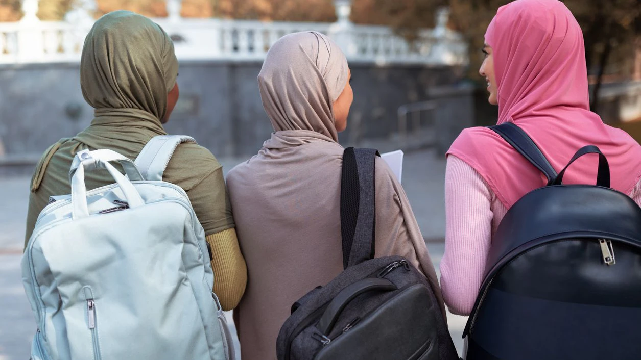Three Unrecognizable Muslim Students Ladies With Backpacks Walking Back To Camera In Park Outdoor. University Education And Lifestyle, Study And Degree For Modern Arab Female Women Concept. Rear View