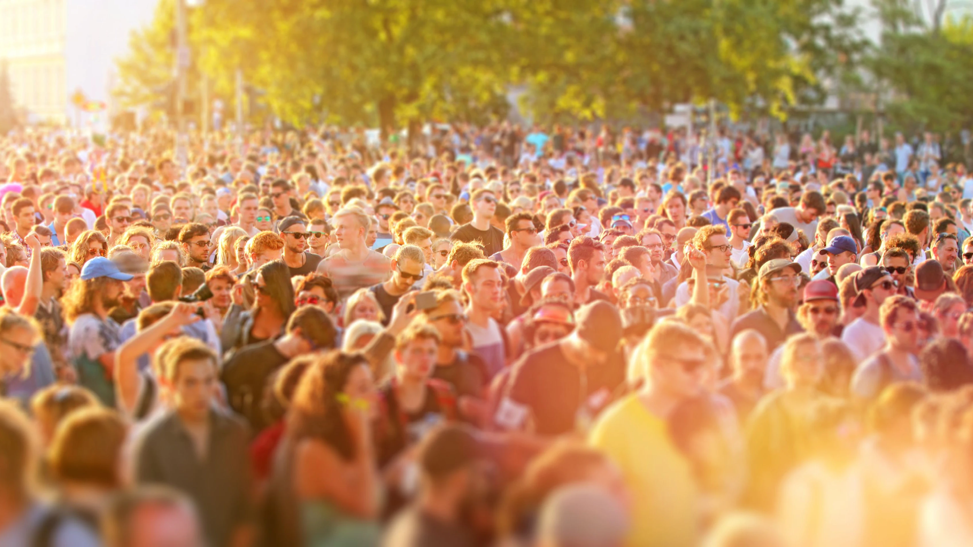 Large crowd of young people crowding city streets in a sunny day during a music festival, walking, dancing and having fun. Street parties are a common way for teenagers to entertain together during the summer in Berlin. Warm sunlight with lens flare. Wideangle horizontal image.