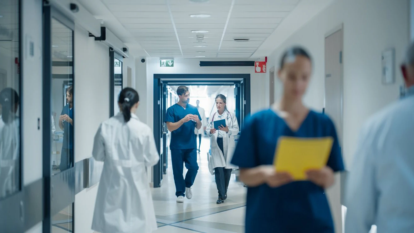 Hospital Hallway with Multiethnic Medical Staff Walking to Their Workplaces. Male and Female Colleagues Discussing Healthcare Practices, Using Tablet, Planning Upcoming Clinical Research