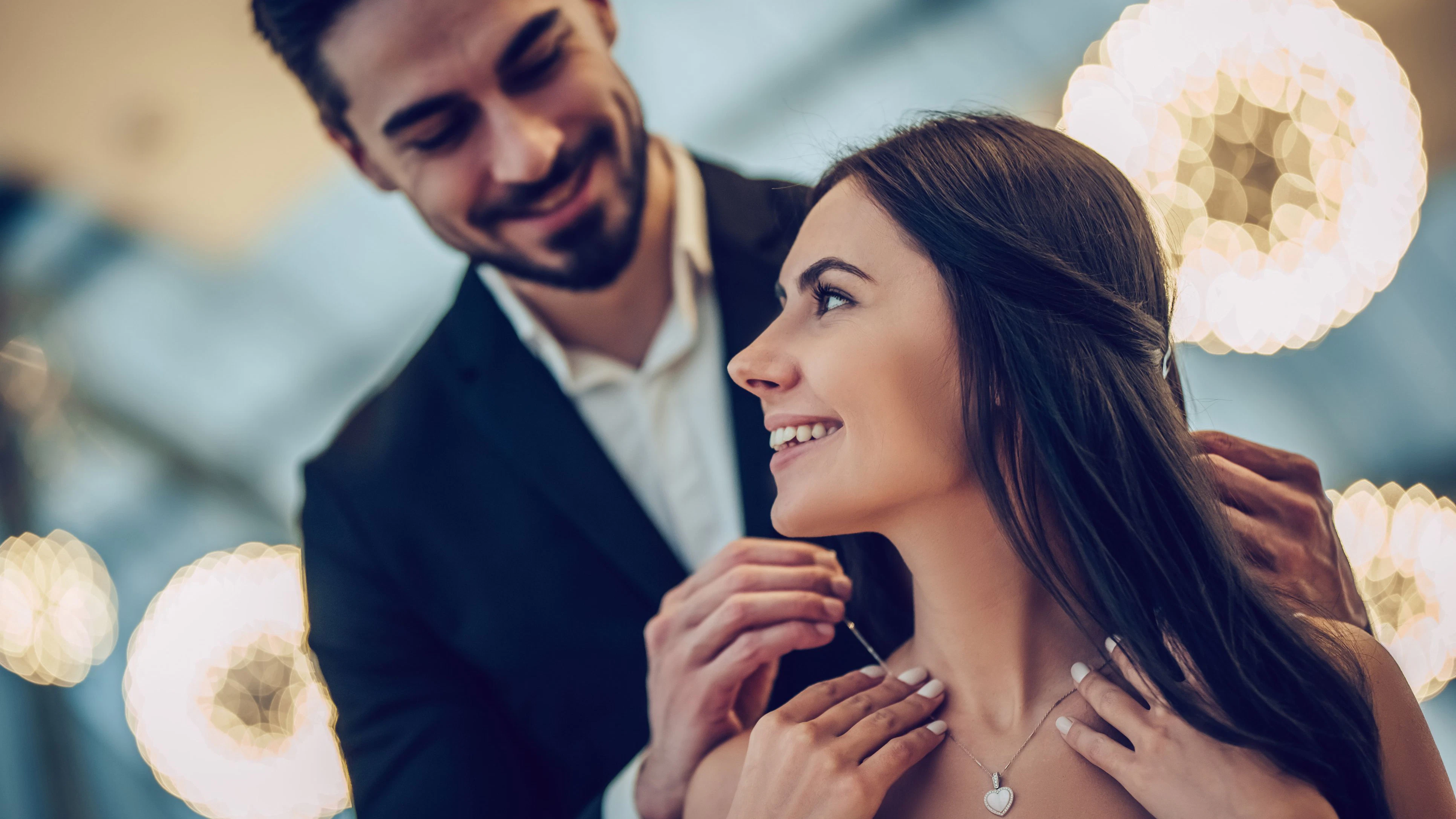 Beautiful loving couple is spending time together in modern restaurant. Attractive young woman in dress and handsome man in suit are having romantic dinner. Celebrating Saint Valentine's Day.